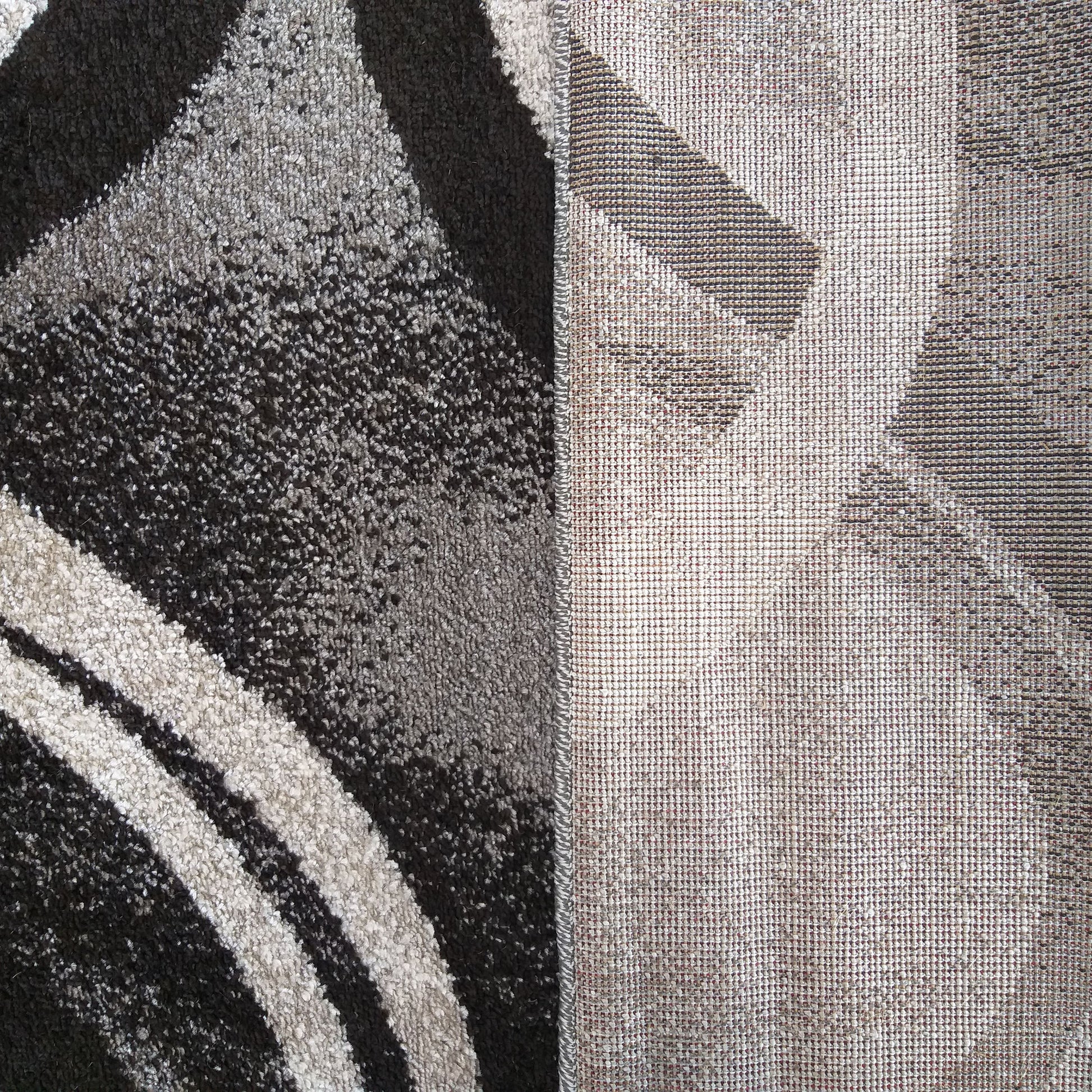 Un tapis au motif abstrait noir, gris et blanc cassé, avec une texture douce et épaisse. La partie retournée du tapis révèle son envers tissé beige