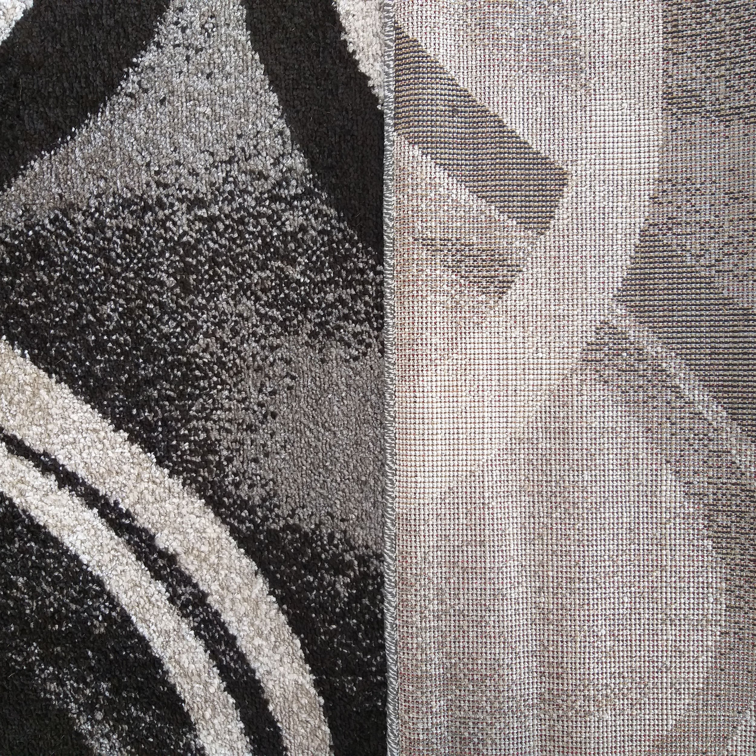 Un tapis au motif abstrait noir, gris et blanc cassé, avec une texture douce et épaisse. La partie retournée du tapis révèle son envers tissé beige