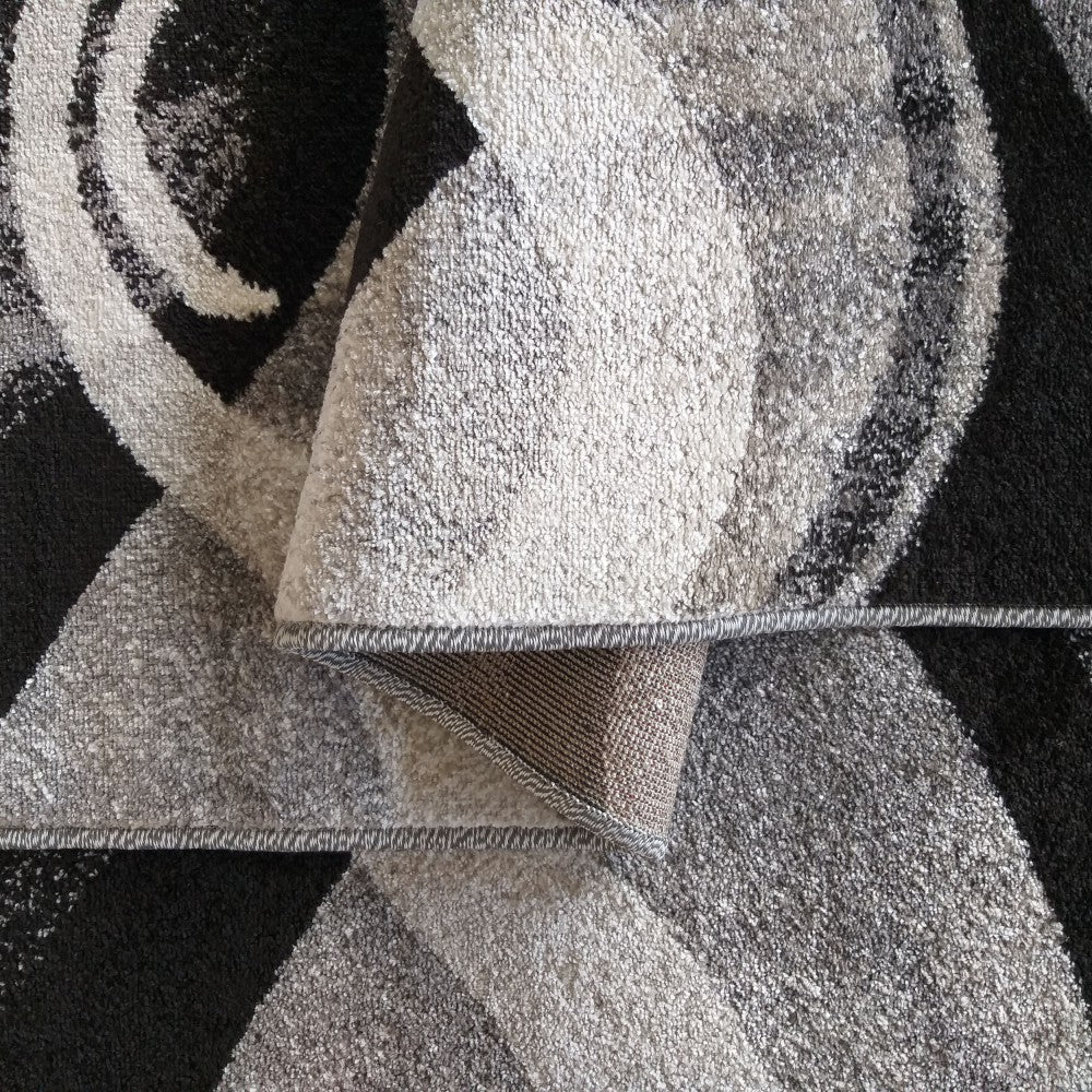 Tapis texturé aux motifs abstraits noirs, blancs et gris. Une section est repliée, révélant la sous-face tissée