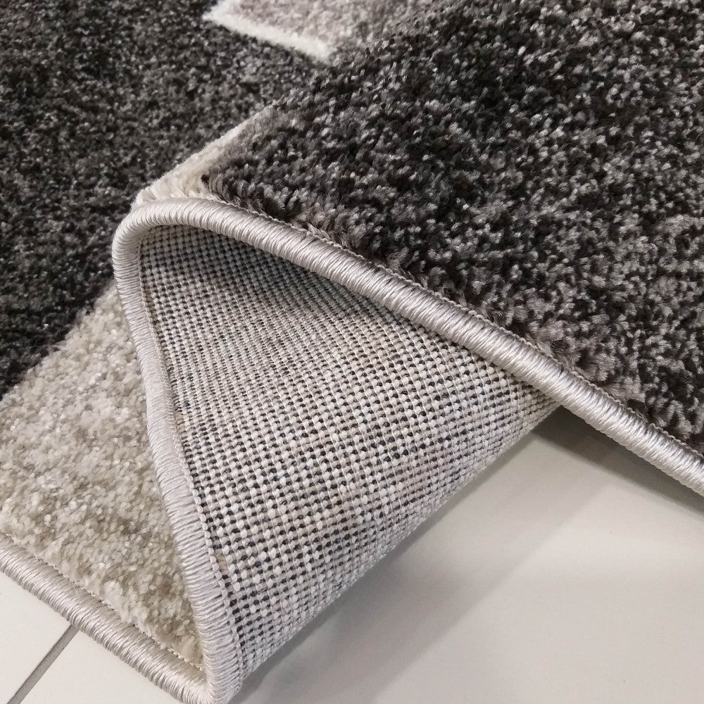 Tapis à poils longs aux motifs géométriques gris foncé, gris clair et blanc cassé, un coin replié révélant le dos tissé