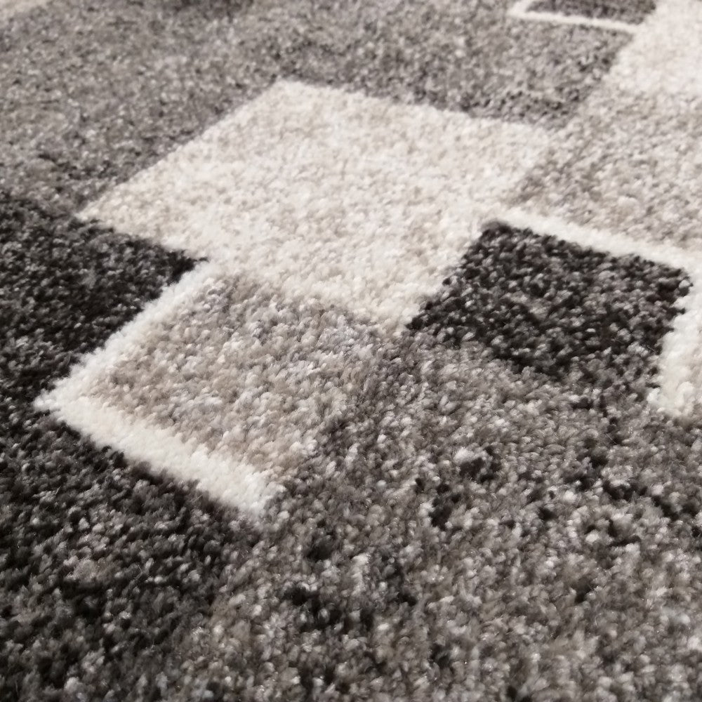 Tapis doux à motifs géométriques, avec des blocs de teintes grises variées, du foncé au très clair