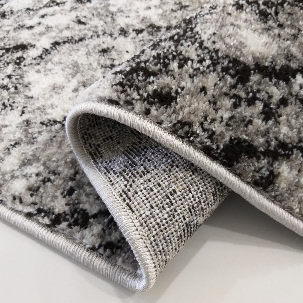 Un tapis doux à poils longs, aux motifs abstraits marbrés gris, noir et blanc, avec un bord surpiqué et son envers visible