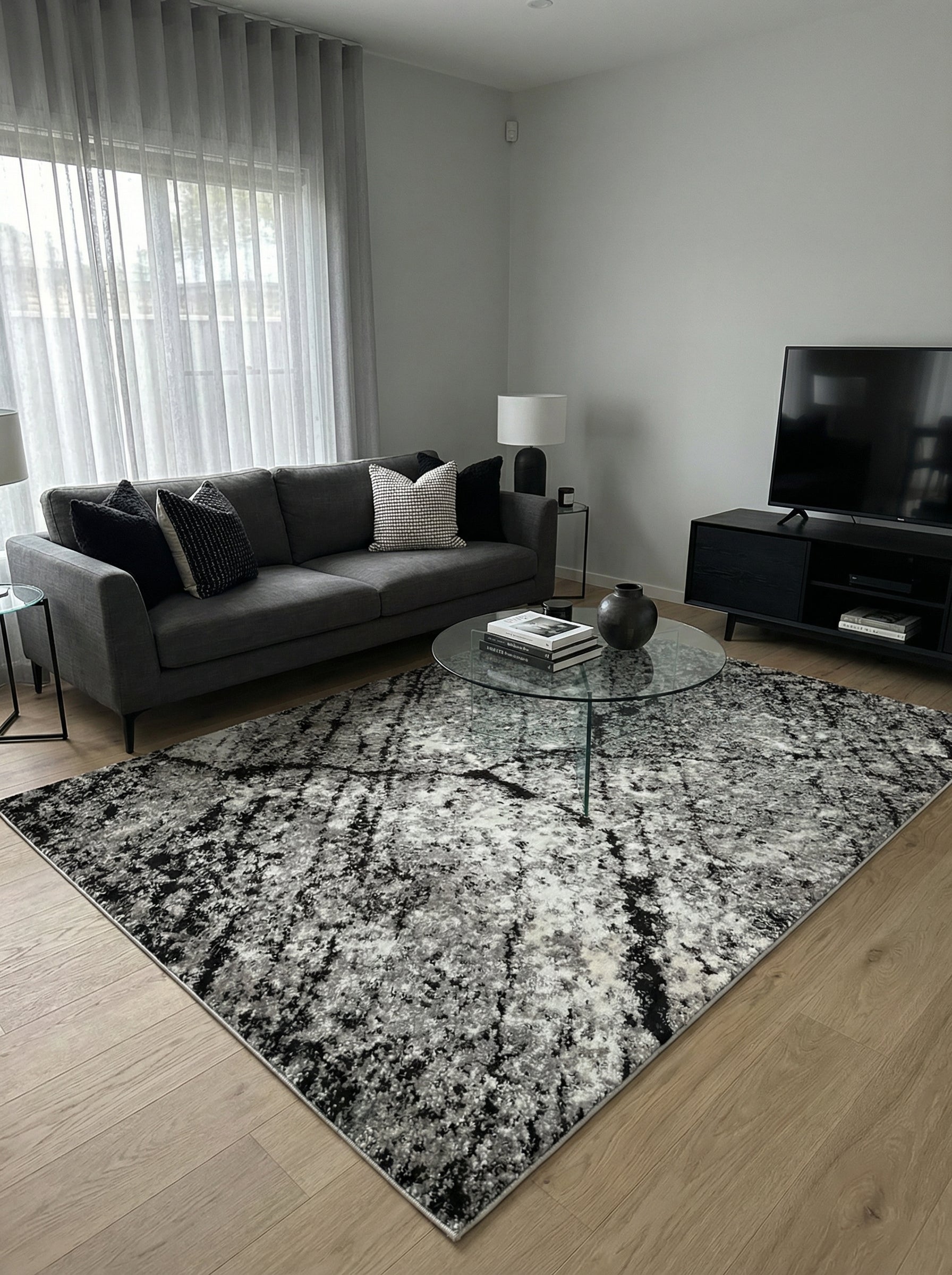 Tapis rectangulaire à motifs abstraits noirs, gris et blancs, créant un effet texturé et patiné sur un sol en bois clair d'un salon