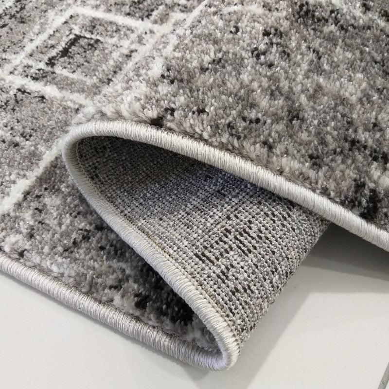 Tapis gris clair et foncé à motifs géométriques blancs, avec une texture douce et un revers tissé apparent