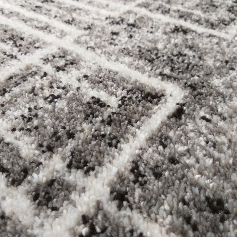 Gros plan d'un tapis moelleux aux motifs géométriques clairs sur un fond moucheté gris, blanc et noir