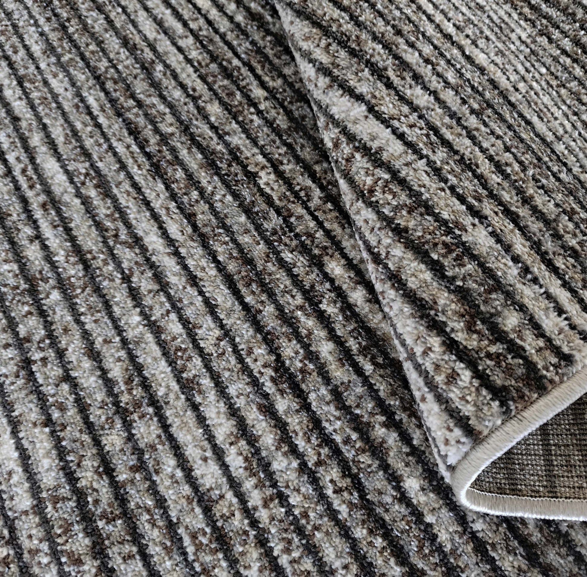 Tapis à poils longs et doux, avec un motif de rayures diagonales beige, marron et noir, un coin est replié