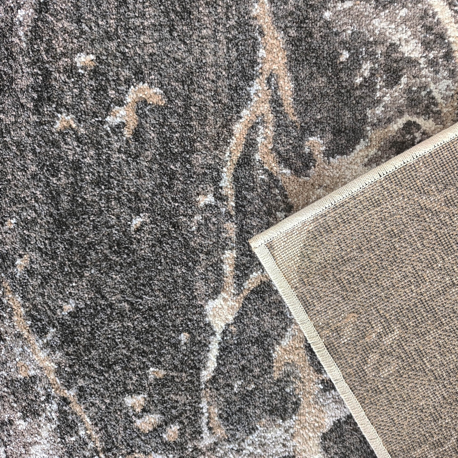 Tapis texturé gris anthracite avec des motifs abstraits beiges et blancs, le dessous tissé est visible