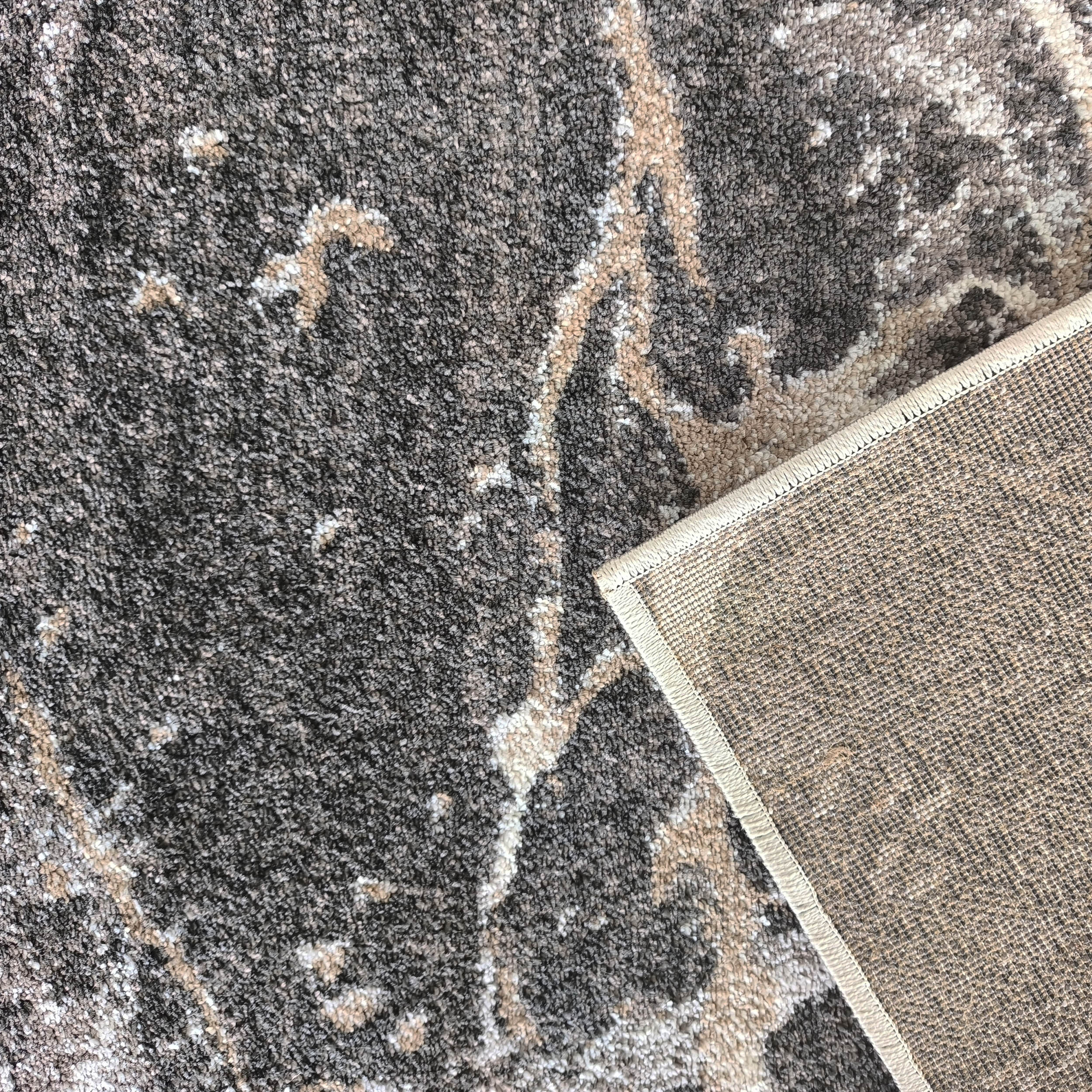 Tapis texturé gris anthracite avec des motifs abstraits beiges et blancs, le dessous tissé est visible