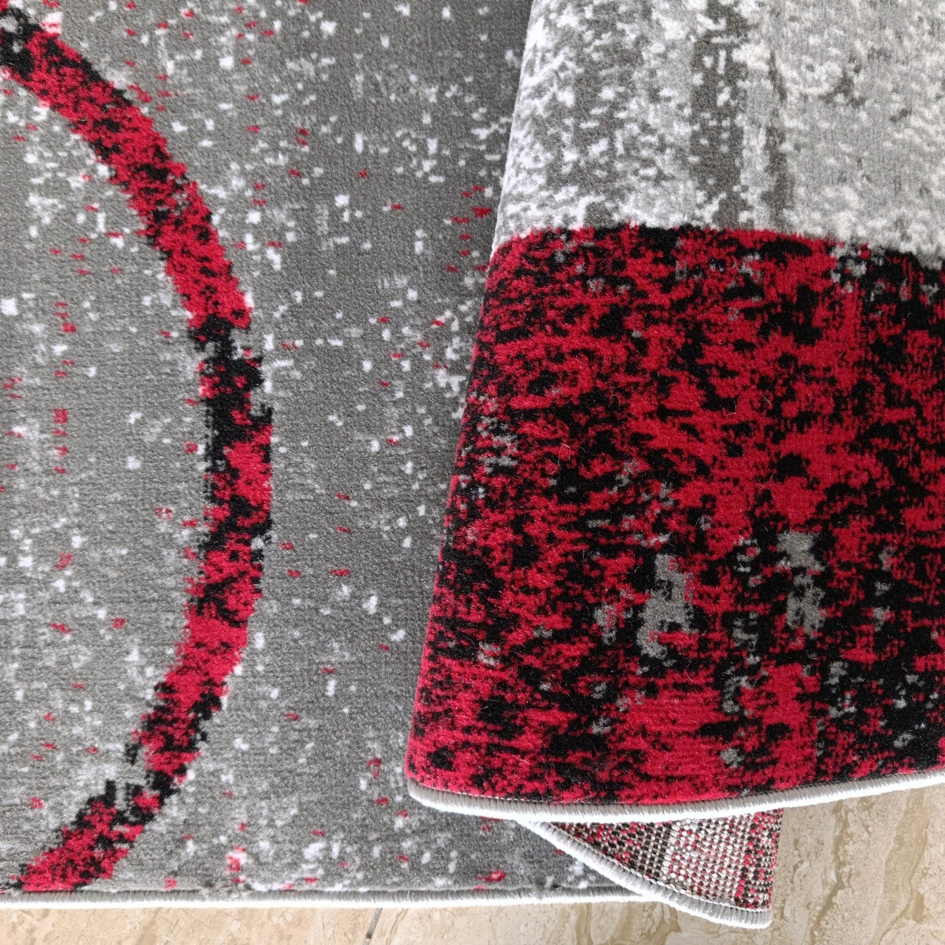 Tapis moucheté gris, rouge, noir et blanc, avec un grand arc rouge, partiellement roulé sur sol clair