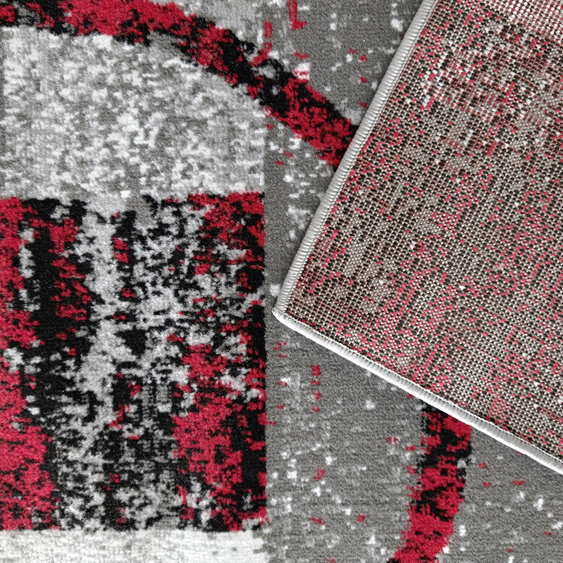 Tapis moelleux motifs rouges, noirs, blancs, gris, montrant envers tissé de points rouges, noirs, gris et bordure claire