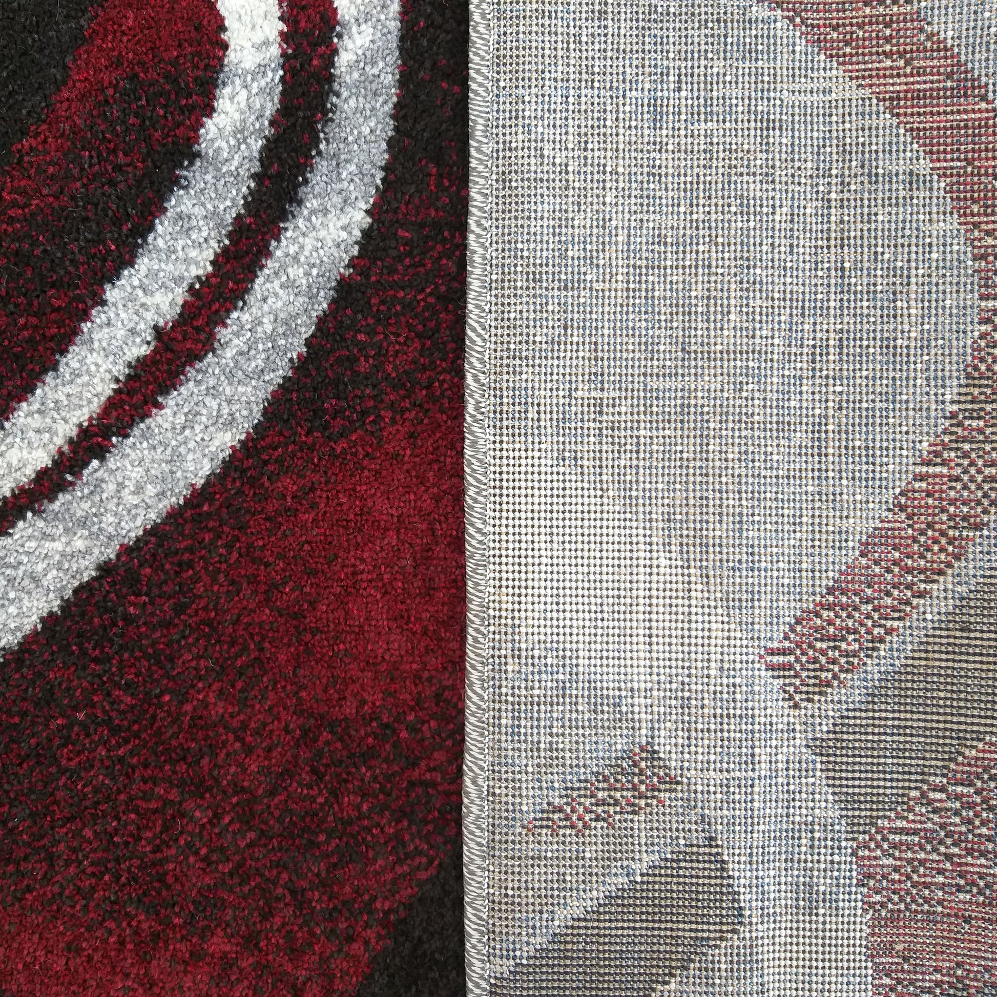 Tapis avec une surface velue rouge, noire et grise à motifs courbes, et un envers tissé gris clair avec des formes colorées