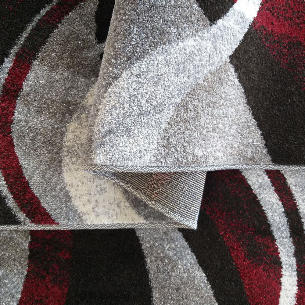 Tapis aux motifs abstraits de vagues grises, bordeaux et noires, à la texture moelleuse, partiellement replié sur lui-même