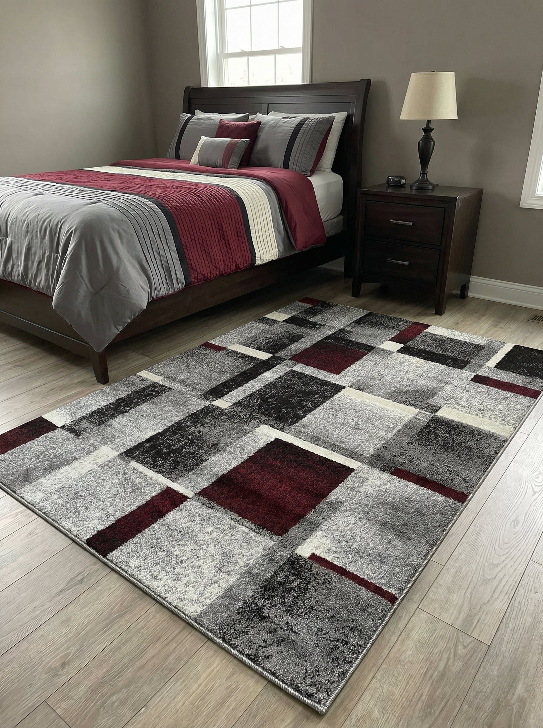 Tapis rectangulaire en matière synthétique aux motifs géométriques gris, noir, blanc et bordeaux, dans une chambre au sol parquet
