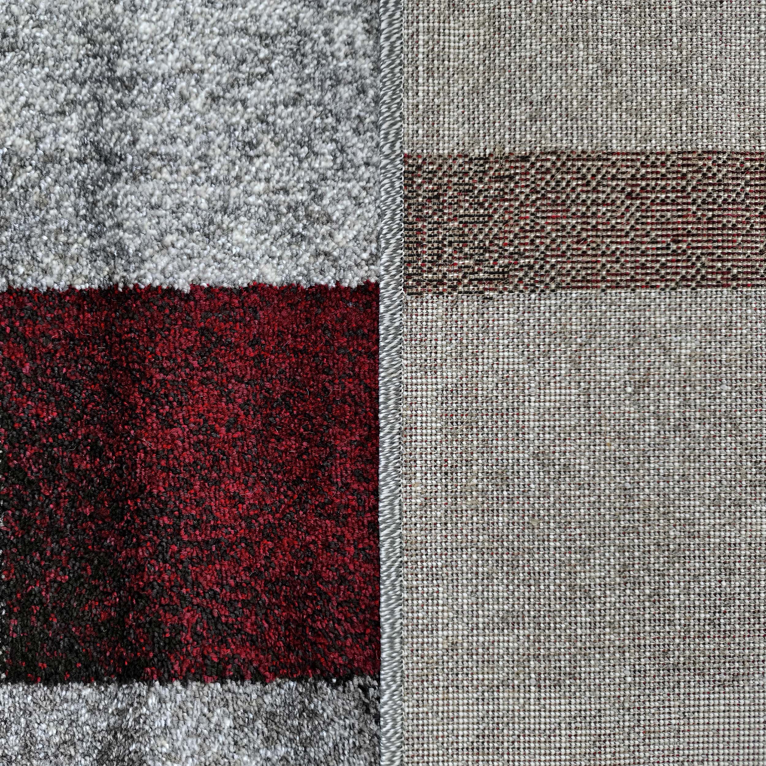 Gros plan sur un tapis présentant le dessus à bandes de poils gris clair et rouge foncé marbré, et l'envers tissé beige avec des motifs