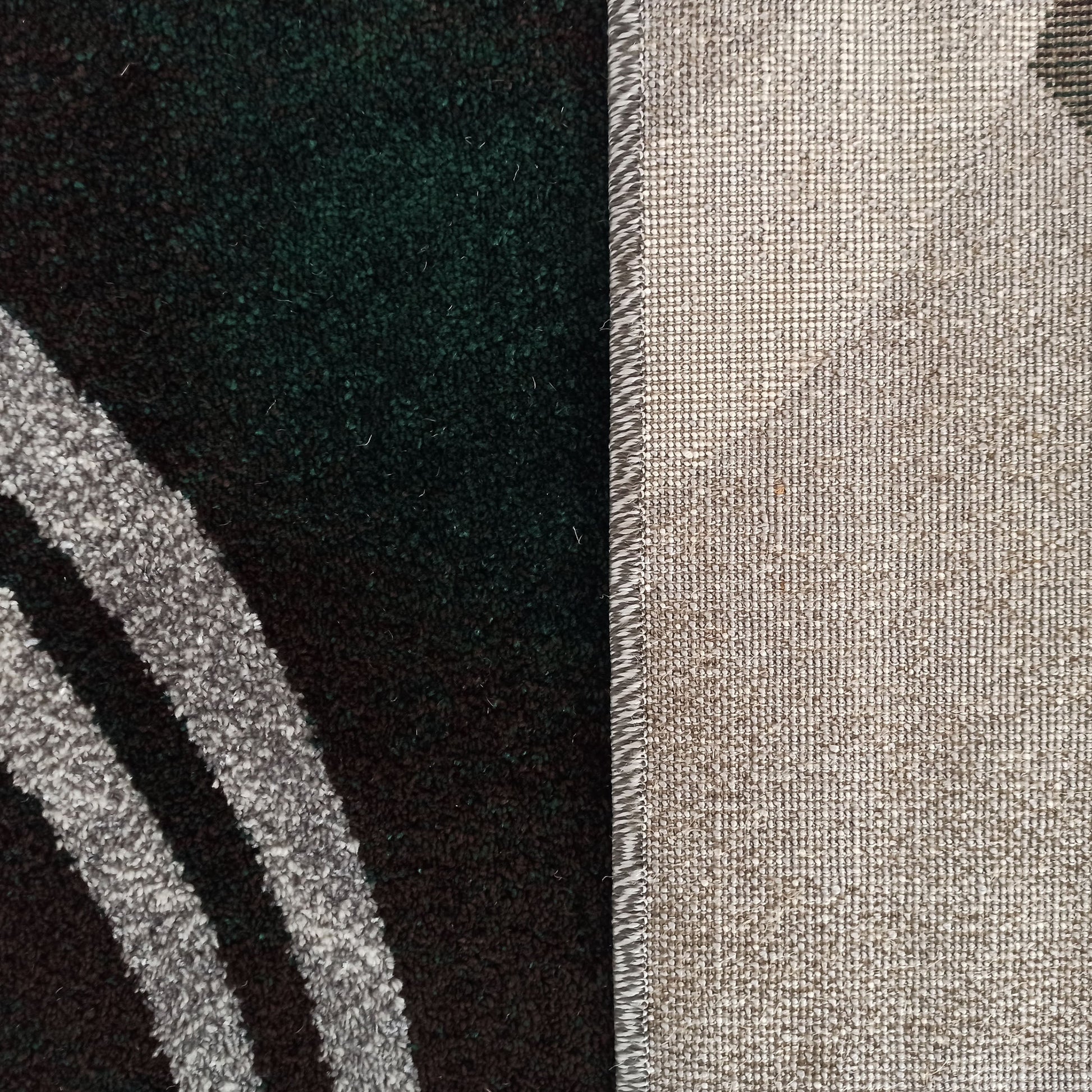 Tapis montrant le côté à poils vert foncé et noir aux bandes grises incurvées, et son envers tissé beige clair