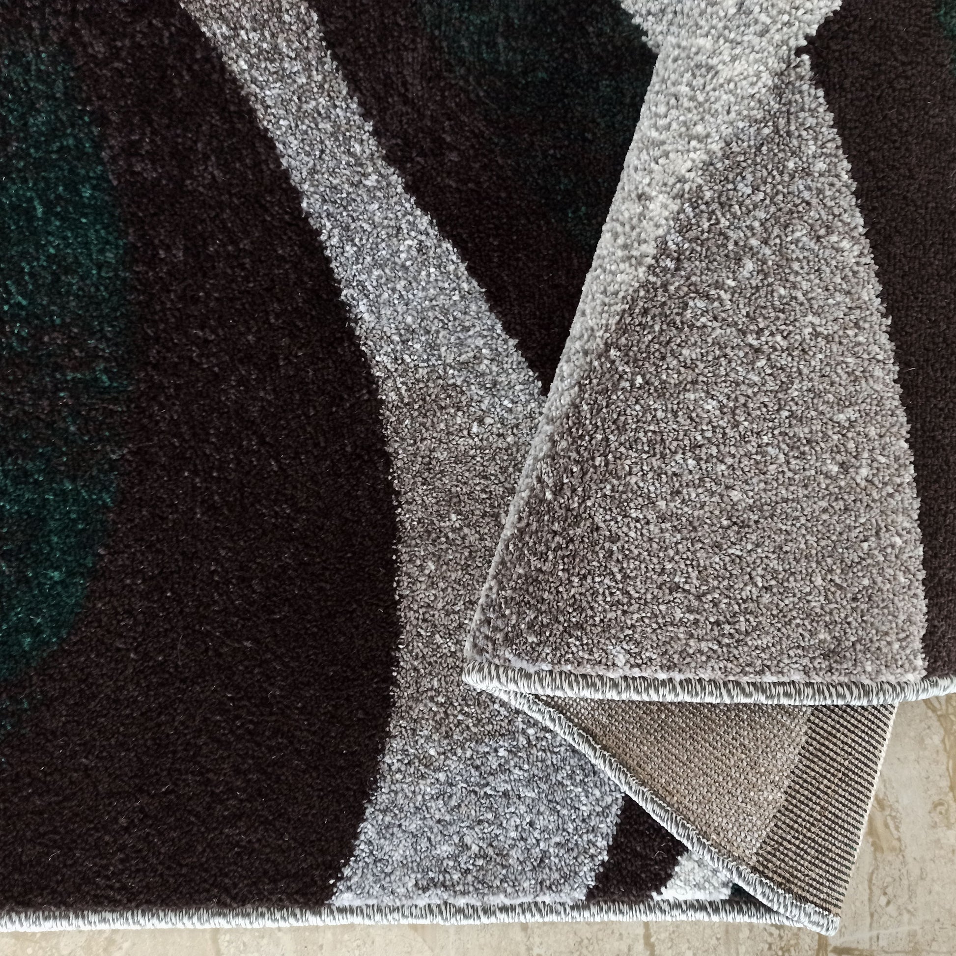 Tapis à poils longs avec motifs ondulés abstraits en brun, gris et vert foncé, un coin est replié pour révéler le revers tissé