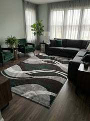 Tapis rectangulaire à motifs abstraits de vagues en vert foncé, marron, gris clair et blanc, posé sur un sol en bois sombre dans un salon moderne