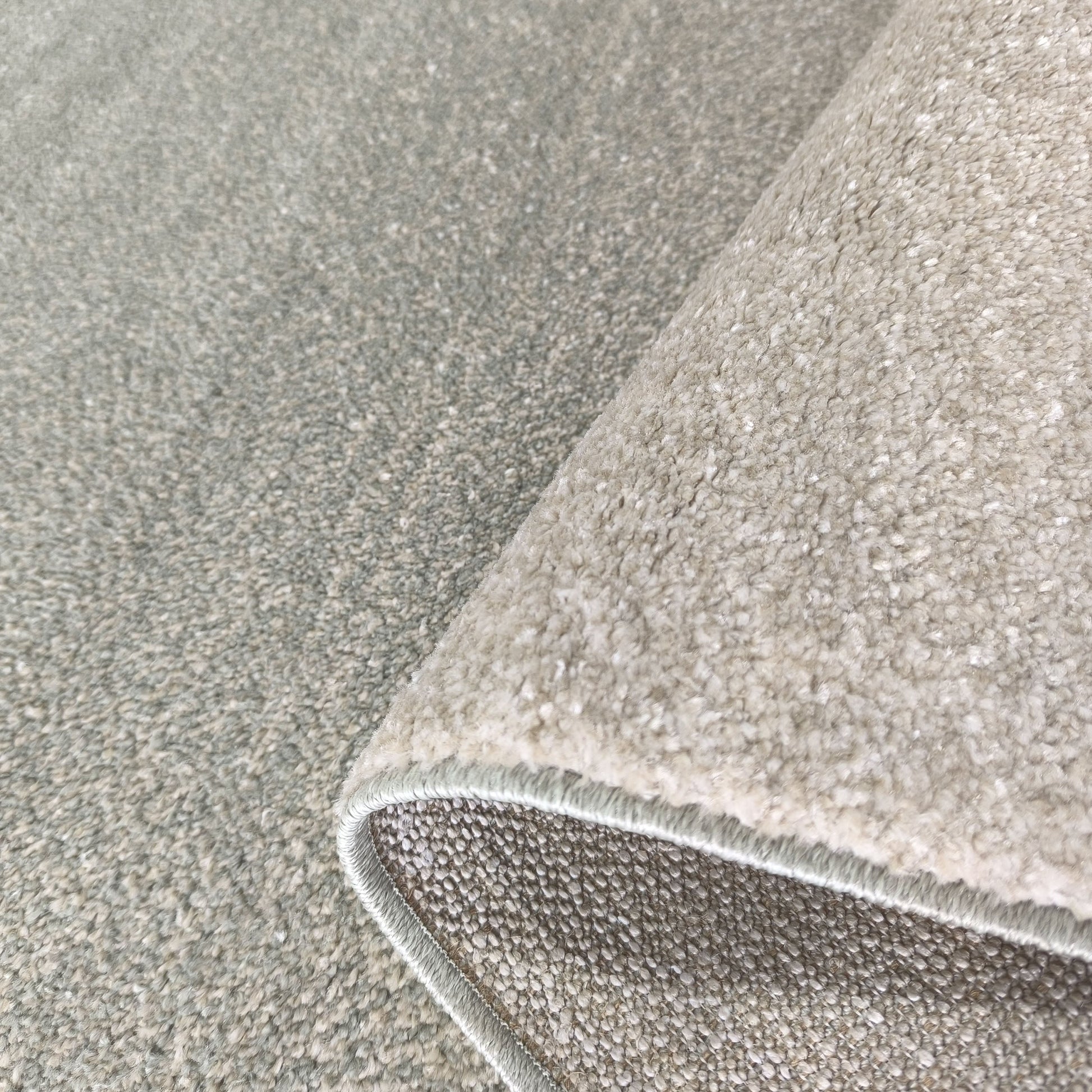 Tapis texturé gris perle et blanc cassé avec un bord roulé, révélant la texture bouclée du dessus et le revers tissé