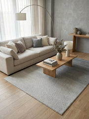 Tapis rectangulaire gris clair à la texture mouchetée, posé sur un parquet en bois clair dans un salon moderne