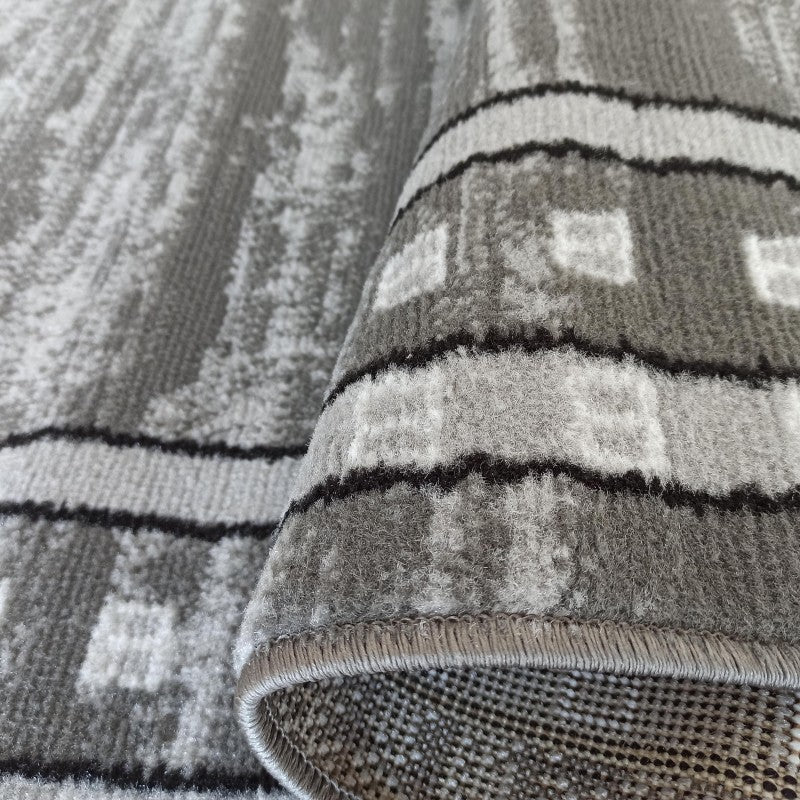 Tapis gris aux multiples nuances, avec motifs abstraits, bandes noires et carrés clairs, de texture douce