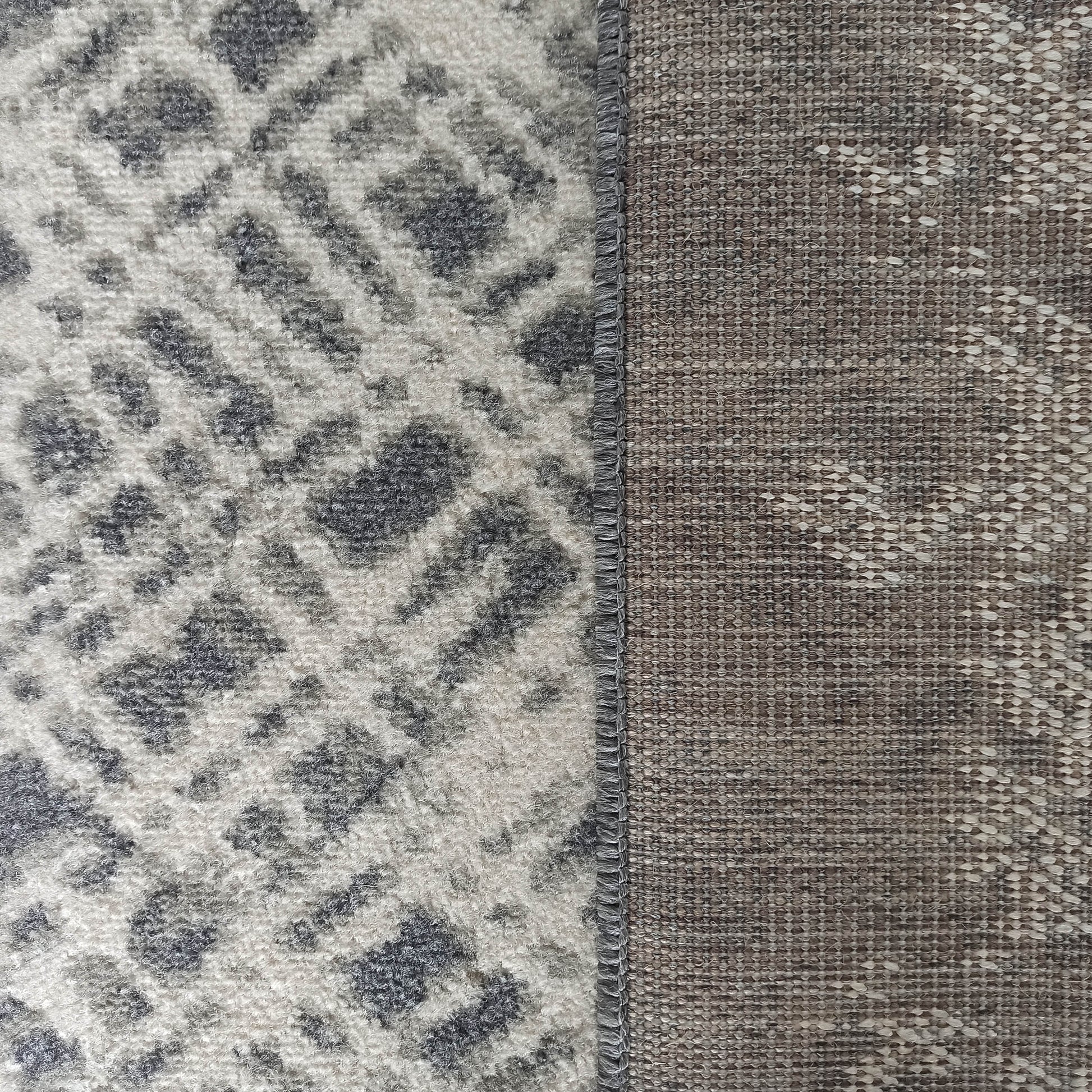 Tapis en gros plan avec une surface veloutée blanc cassé et motifs gris anthracite, et son revers tissé brun chiné