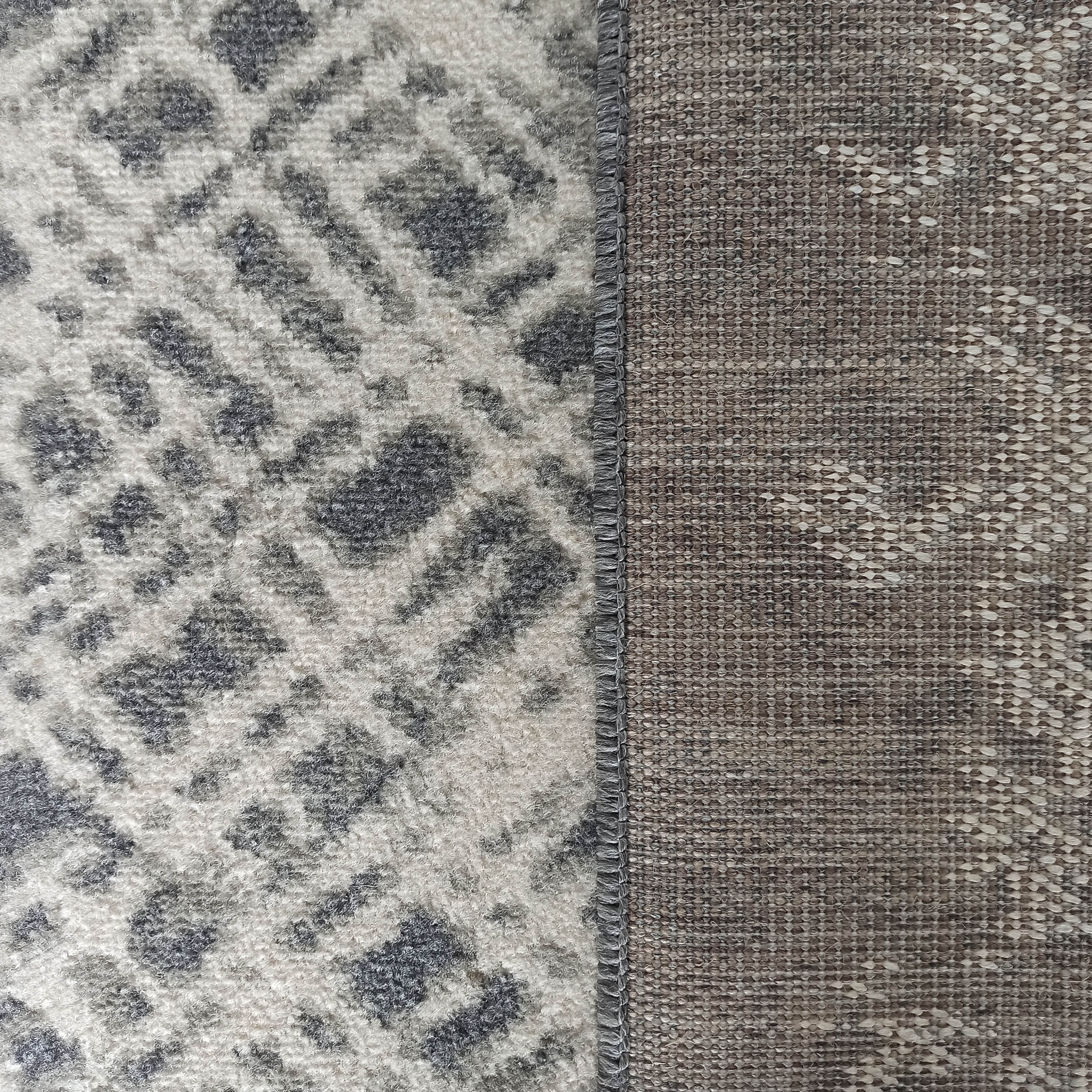 Tapis en gros plan avec une surface veloutée blanc cassé et motifs gris anthracite, et son revers tissé brun chiné