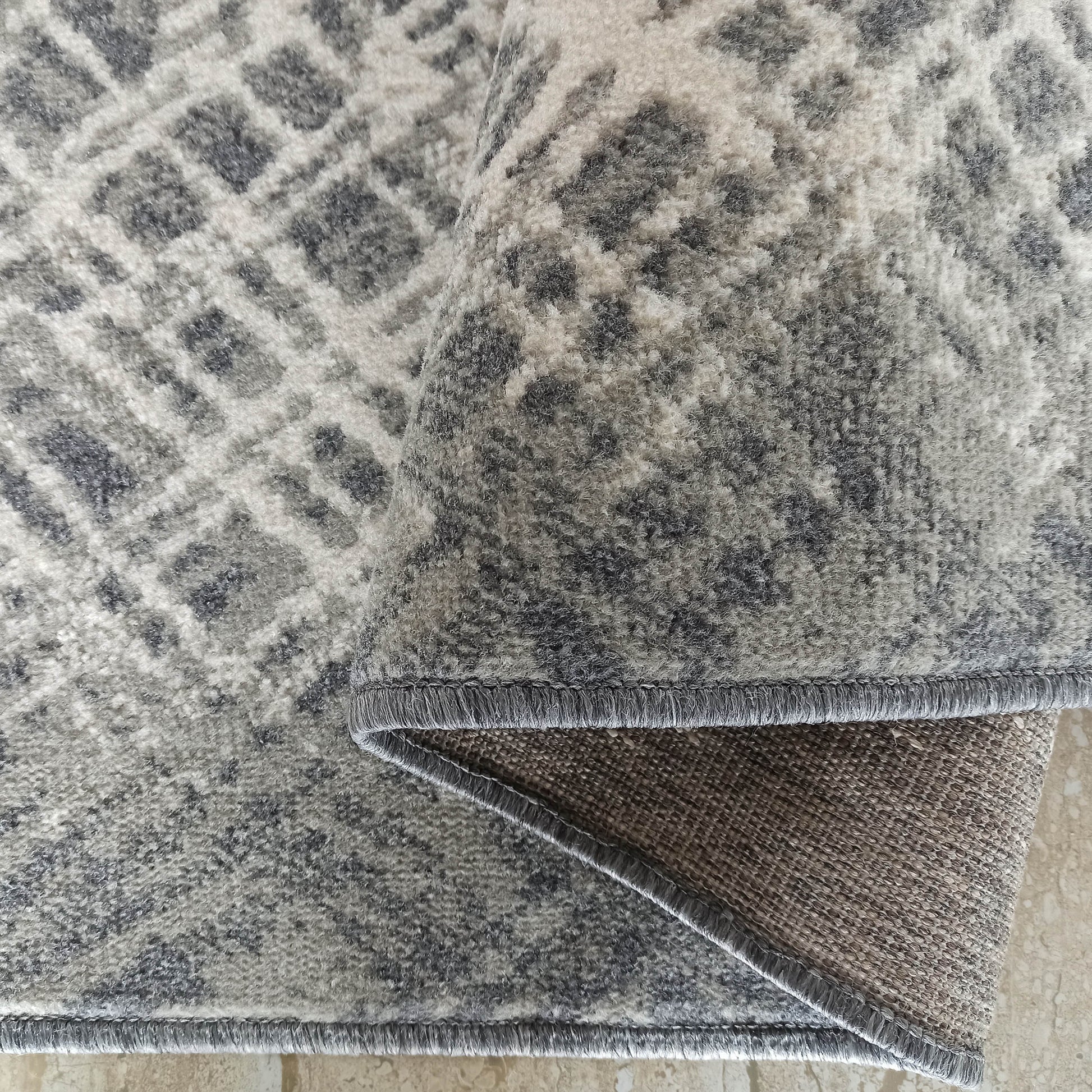 Tapis à poils longs gris et blanc cassé aux motifs marbrés abstraits, partiellement enroulé montrant le dos tissé beige