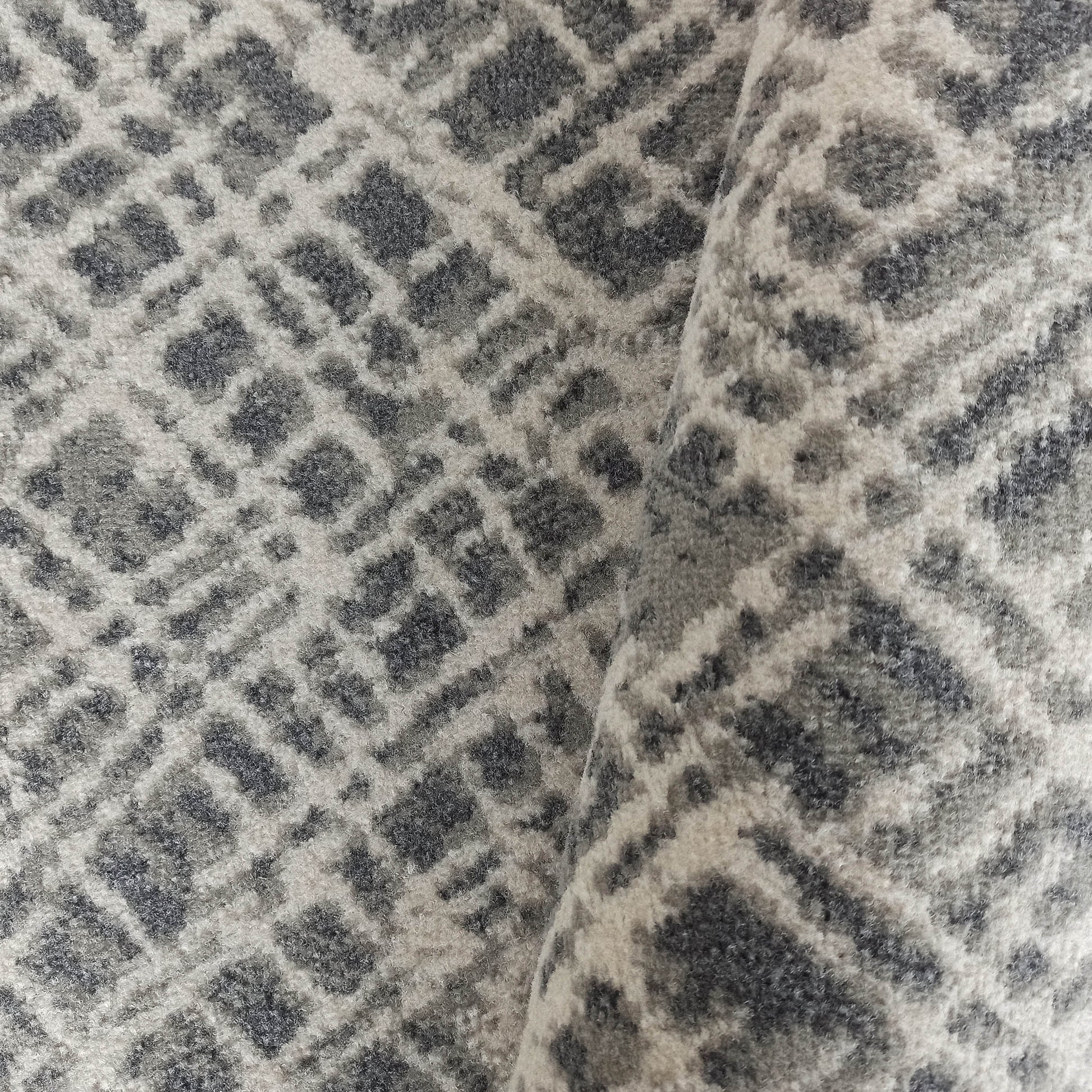 Tapis à poils longs aux motifs géométriques de losanges en nuances de gris et blanc cassé, avec un pli