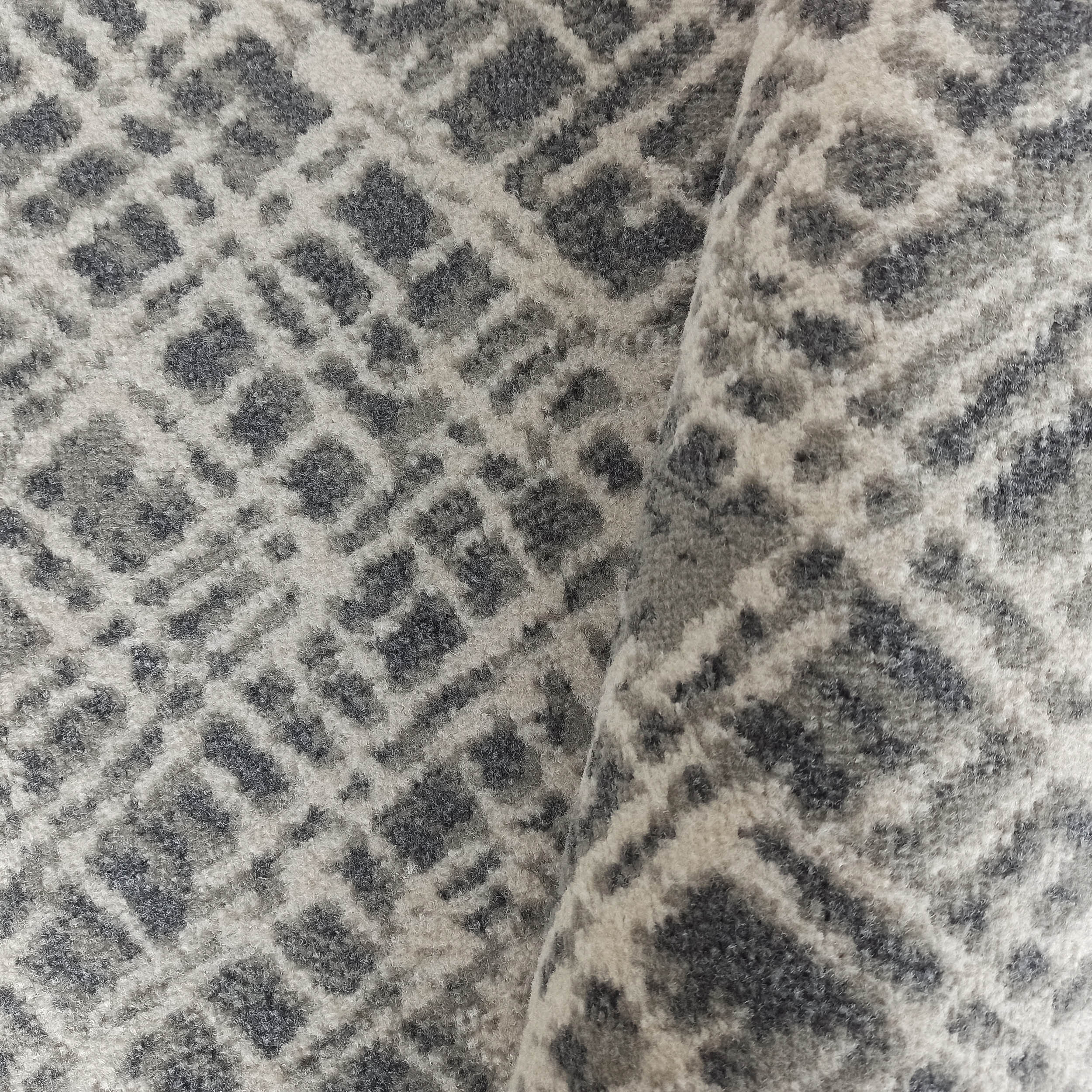 Tapis à poils longs aux motifs géométriques de losanges en nuances de gris et blanc cassé, avec un pli