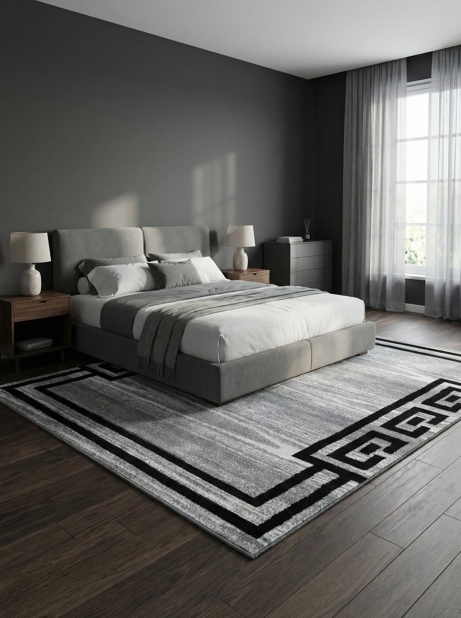 Tapis rectangulaire gris et blanc aux motifs abstraits et bordure géométrique noire, posé sur un parquet foncé dans une chambre moderne