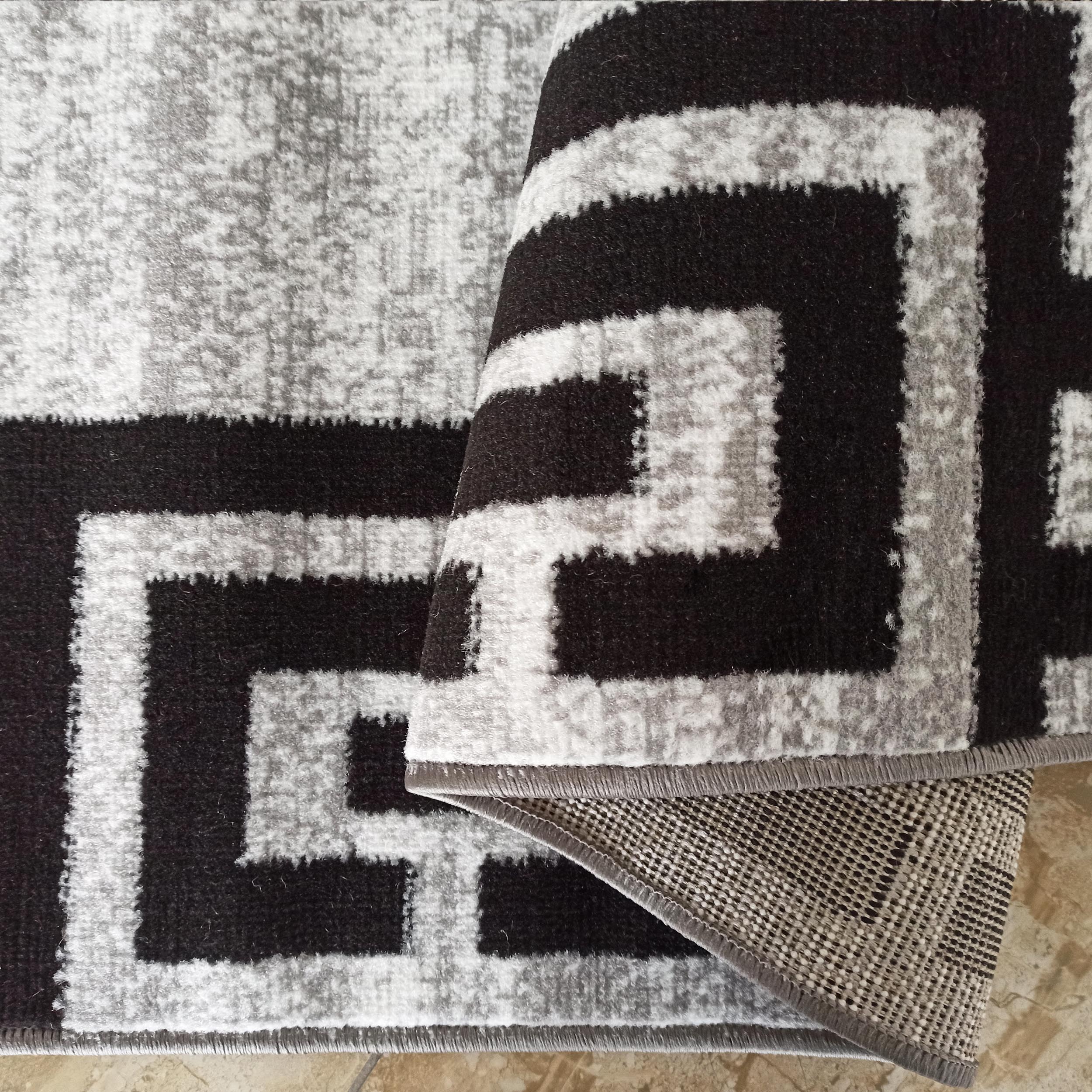 Tapis plié aux motifs géométriques angulaires noir, blanc et gris chiné. Le dessus est en fibres douces, le dessous en matière tissée