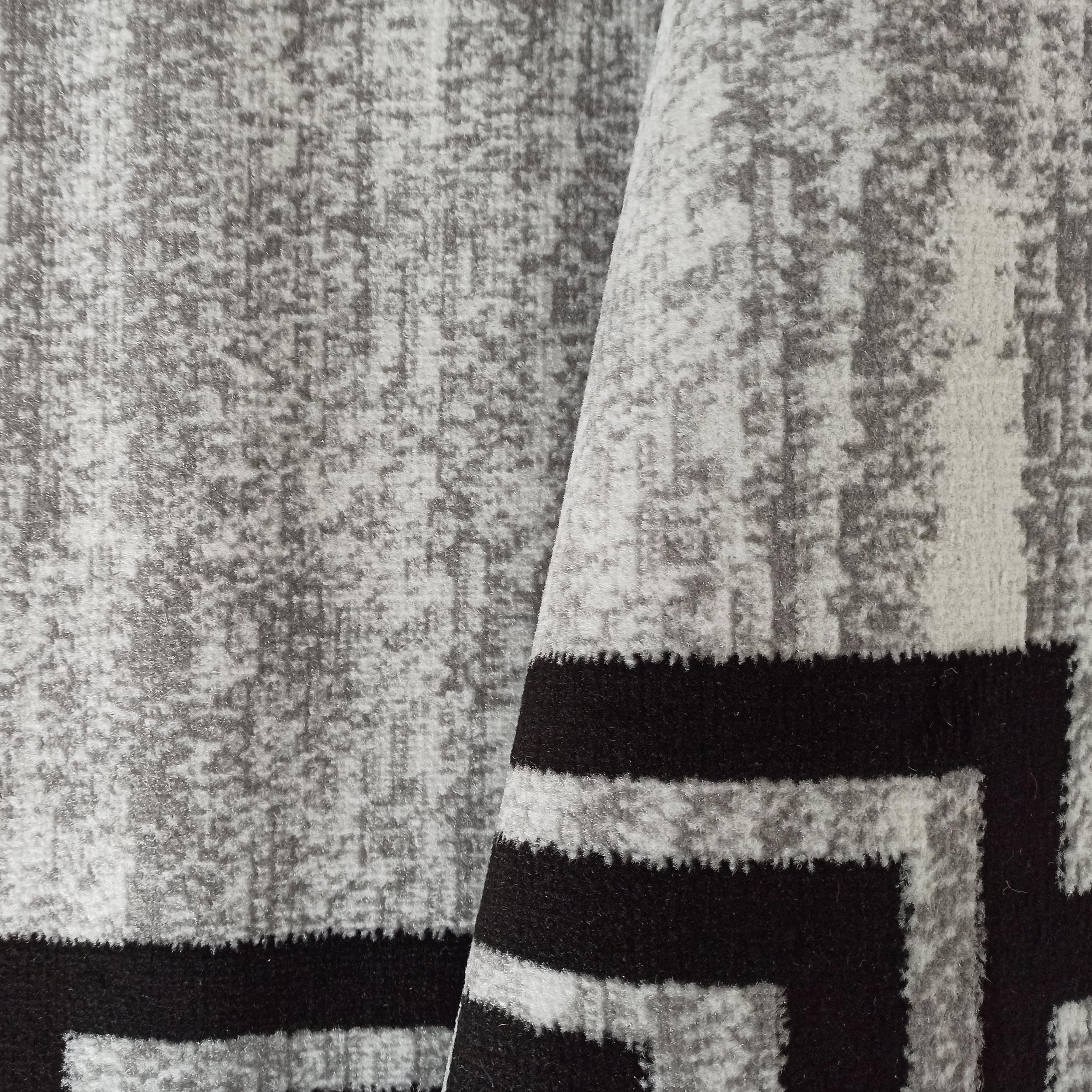 Tapis plié aux motifs abstraits mouchetés gris et blancs, avec des formes géométriques noires nettes