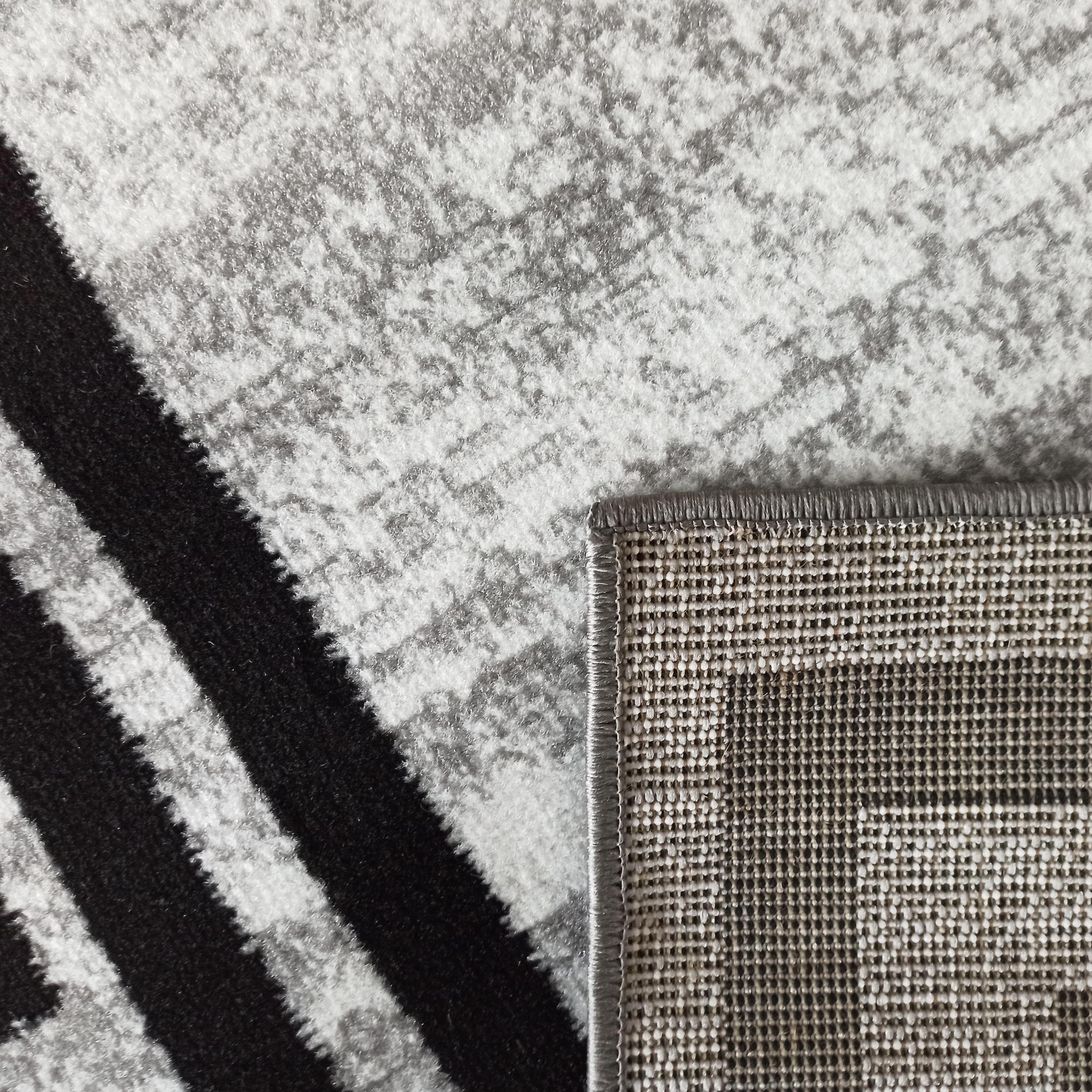 Tapis aux motifs abstraits gris clair et gris foncé, avec de larges rayures noires diagonales et le dessous tissé visible