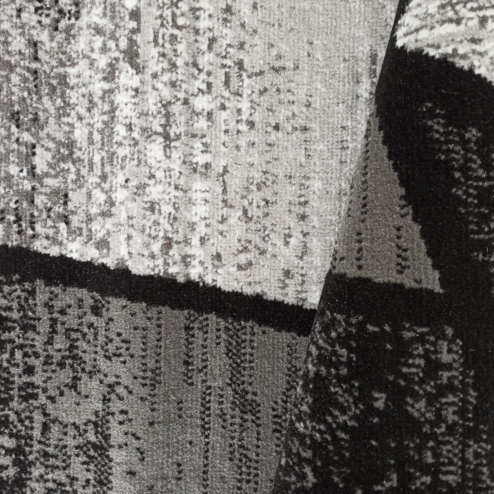 Tapis textile aux motifs abstraits contrastés gris, blancs et noirs, avec une partie pliée sur le côté