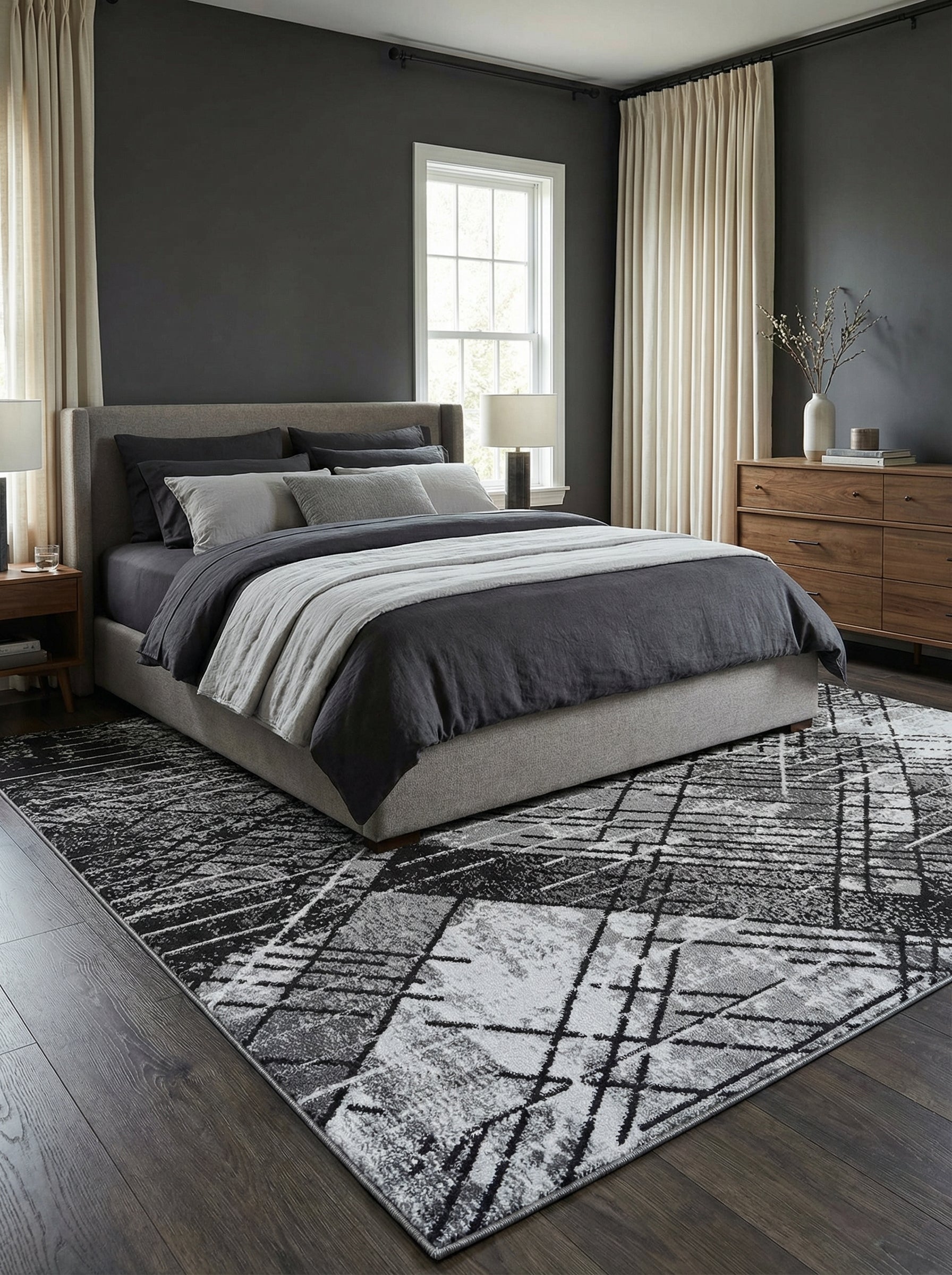 Tapis rectangulaire gris, noir et blanc avec motif géométrique abstrait de lignes et textures diverses, placé dans une chambre