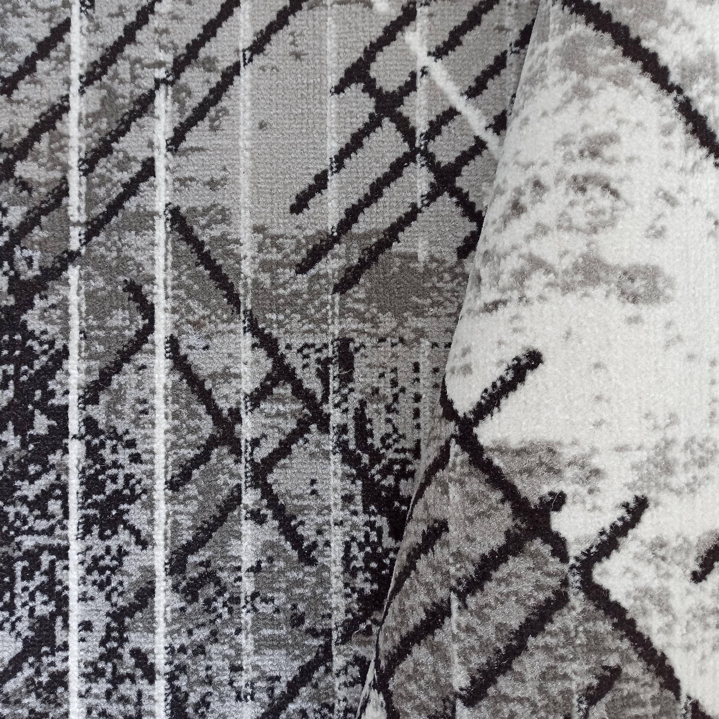 Tapis enroulé présentant des motifs géométriques abstraits en noir, gris et blanc sur une surface texturée de poils