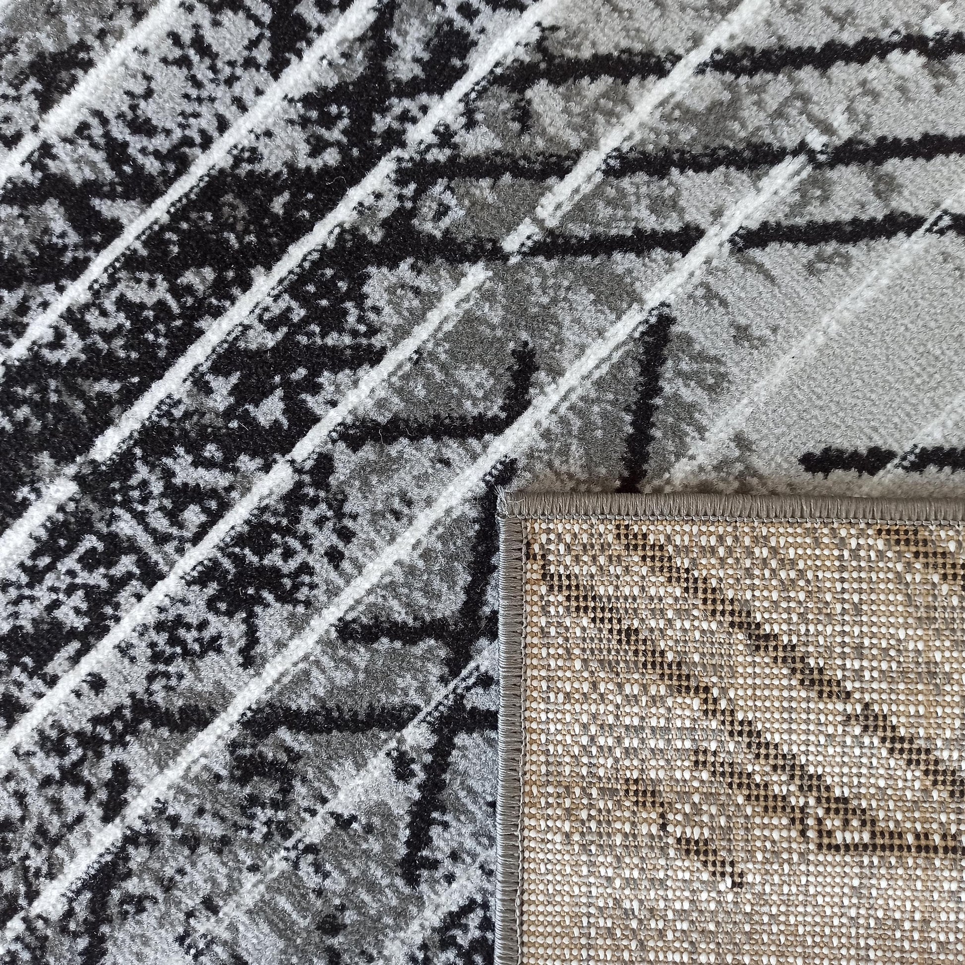Tapis à motifs abstraits noirs, gris et blancs; le revers tissé en beige, blanc et noir est visible sur le côté