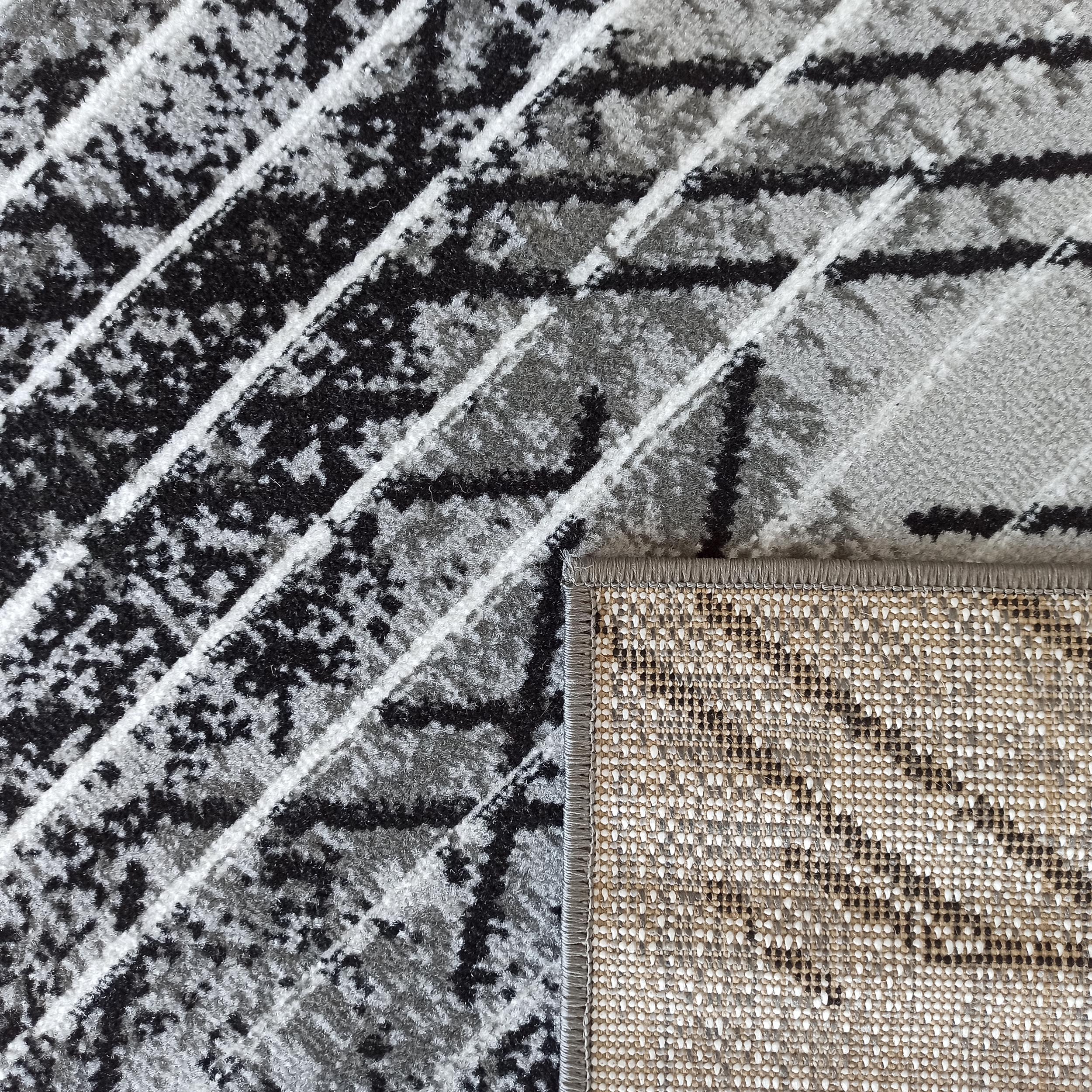 Tapis à motifs abstraits noirs, gris et blancs; le revers tissé en beige, blanc et noir est visible sur le côté