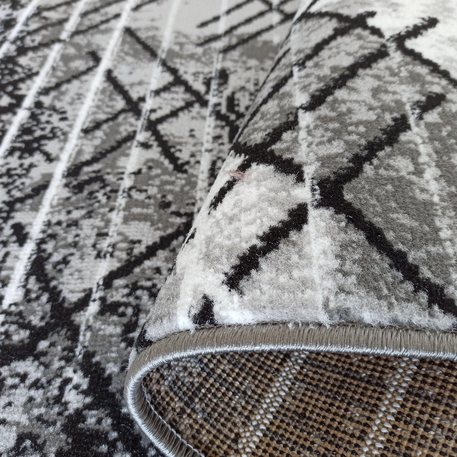 Tapis doux roulé, à motifs géométriques abstraits noirs et gris sur fond blanc, bordure grise et envers tissé beige