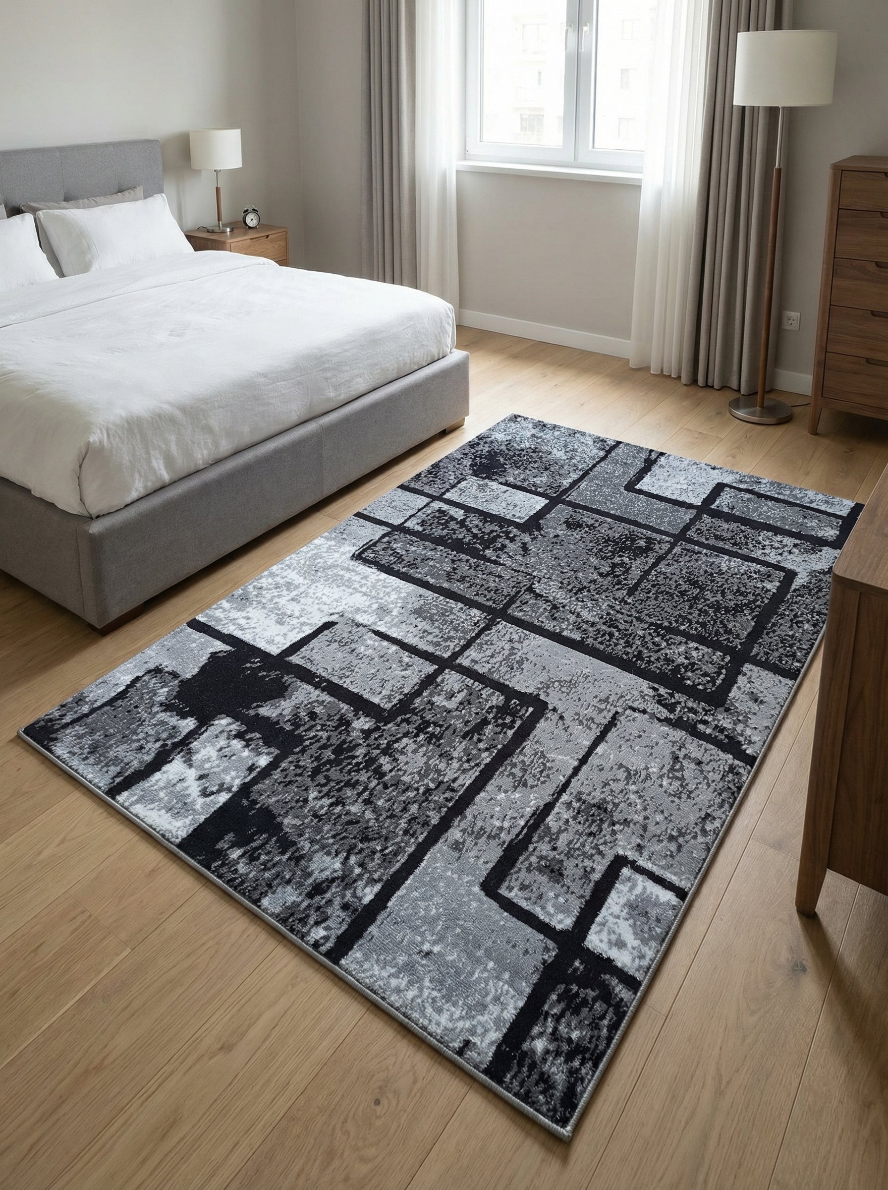 Tapis rectangulaire à motifs géométriques abstraits noirs, gris et blancs, reposant sur un parquet clair dans une chambre