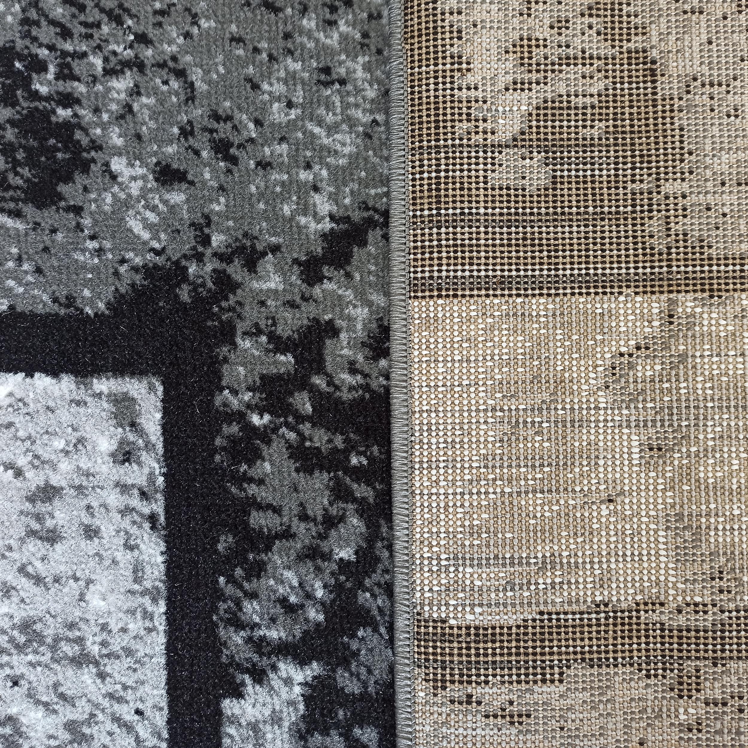 Tapis à motifs abstraits noirs, gris et blancs sur sa face velue, avec revers tissé beige et marron, et couture grise visible