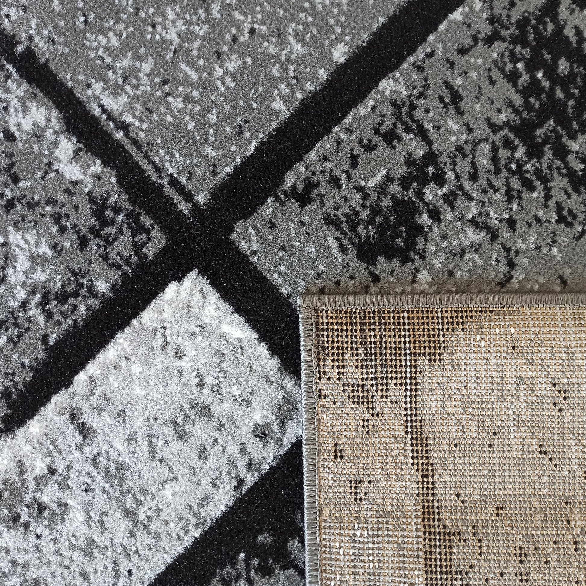 Tapis aux motifs abstraits gris et noirs, avec une texture poilue sur le dessus et un revers tissé beige