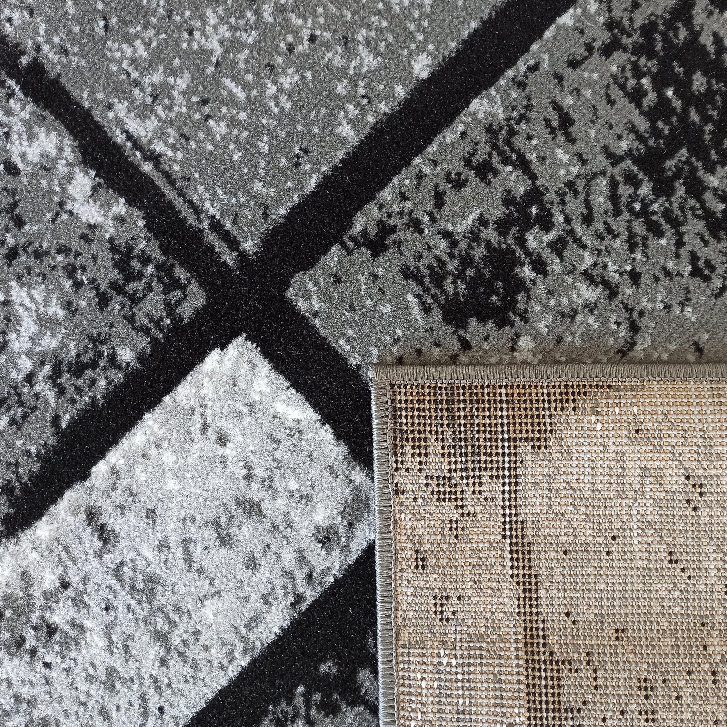 Tapis aux motifs abstraits gris et noirs, avec une texture poilue sur le dessus et un revers tissé beige
