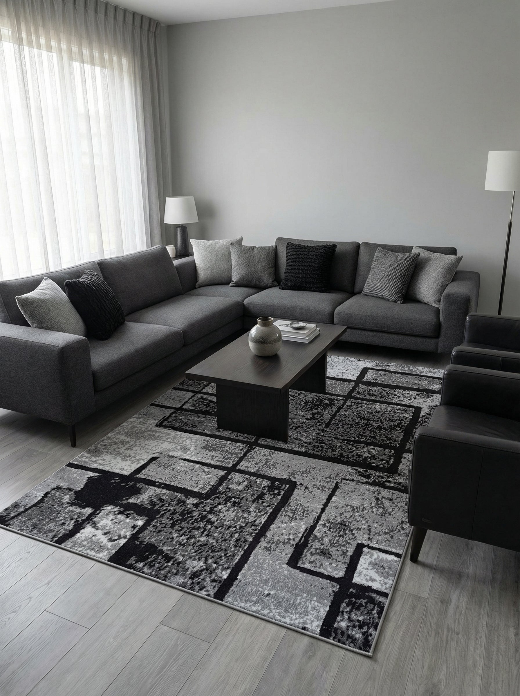 Tapis rectangulaire à motifs géométriques abstraits gris, anthracite et noirs posé sur un sol clair dans un salon moderne