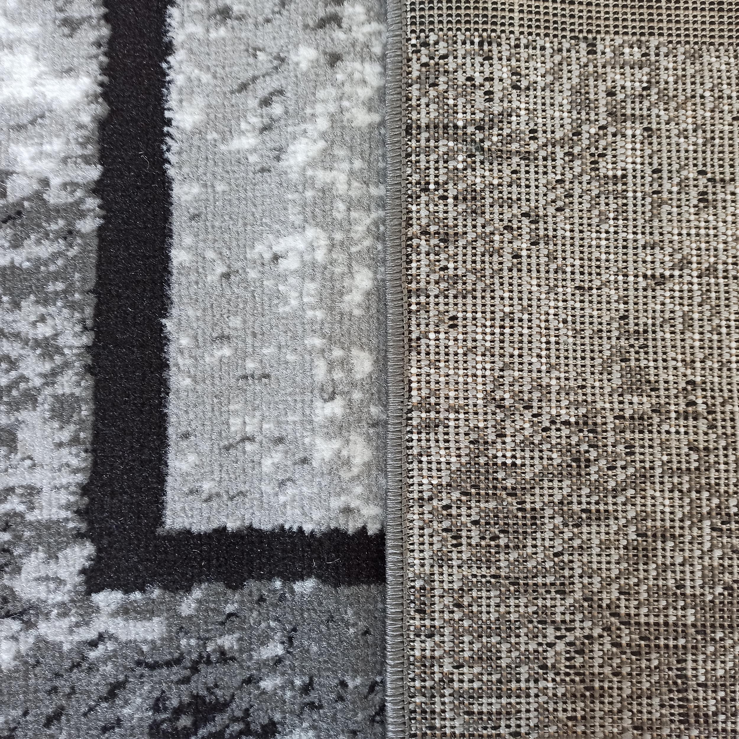 Tapis aux motifs abstraits gris, blanc et noir, montrant sa surface veloutée et son envers tissé beige