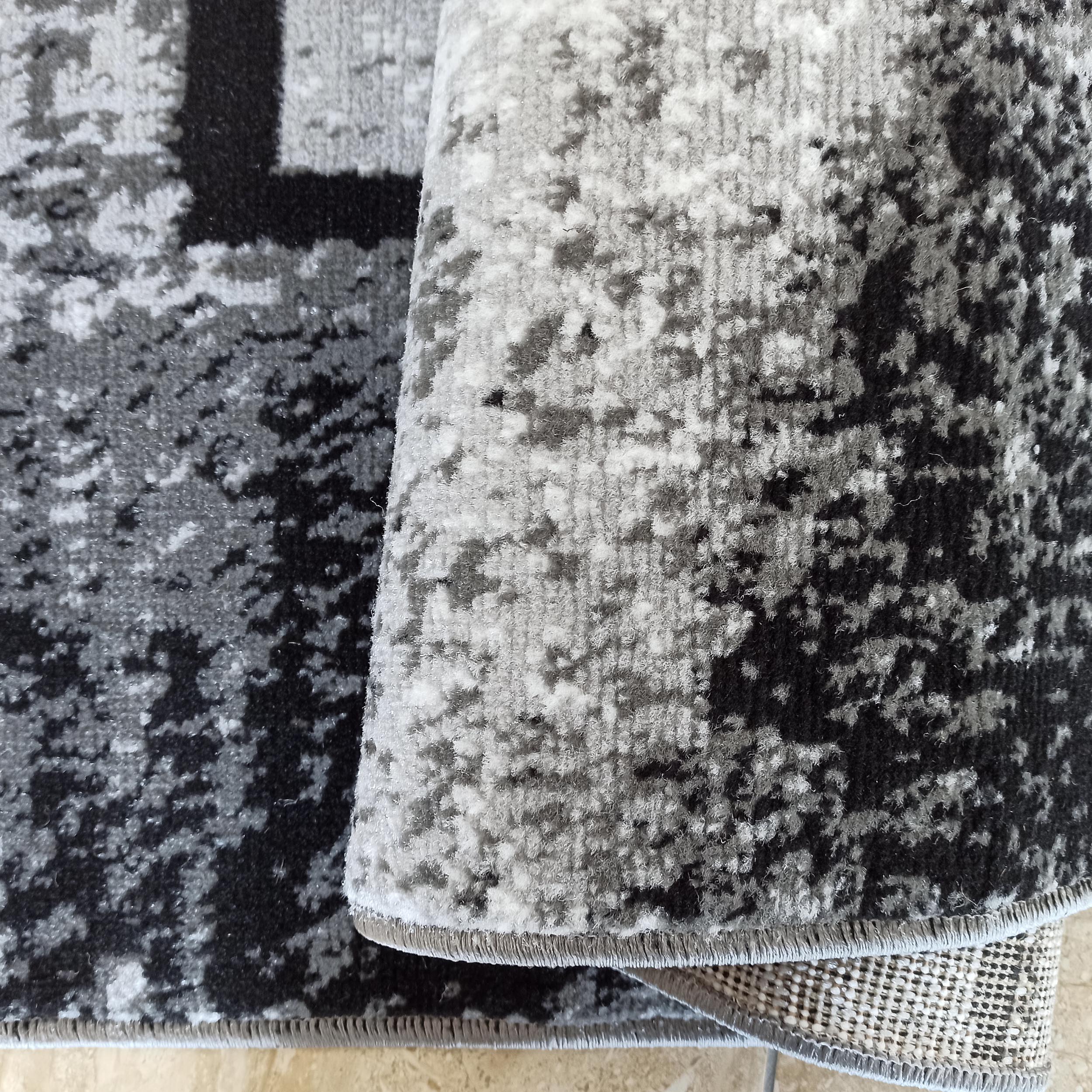 Tapis roulé à motif abstrait moucheté noir, gris et blanc, avec une texture de poils apparents et son envers tissé
