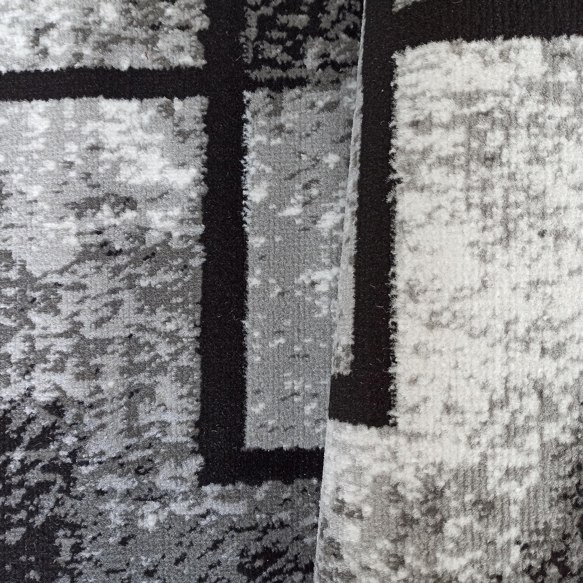 Tapis aux motifs géométriques et abstraits en noir, gris et blanc, avec une texture pelucheuse, partiellement roulé