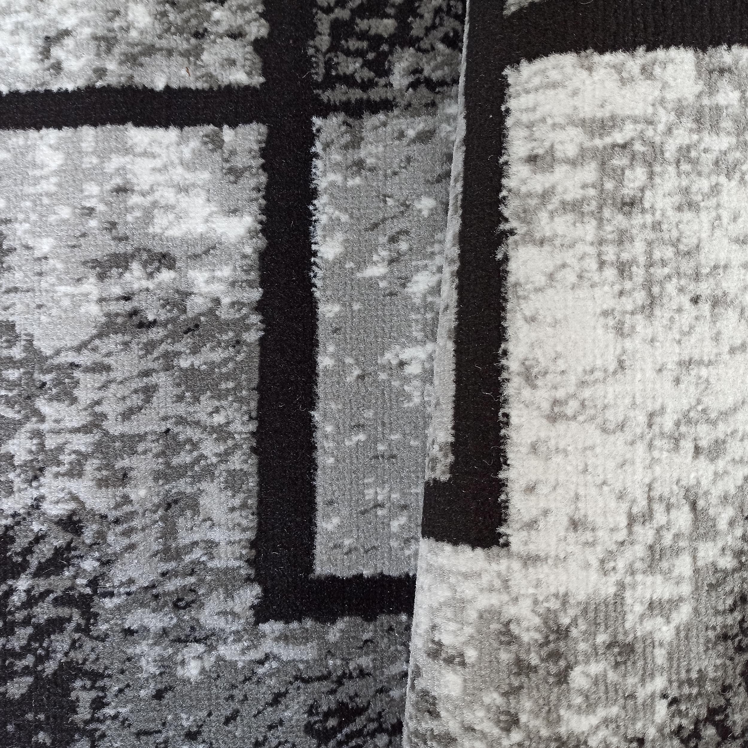 Tapis aux motifs géométriques et abstraits en noir, gris et blanc, avec une texture pelucheuse, partiellement roulé