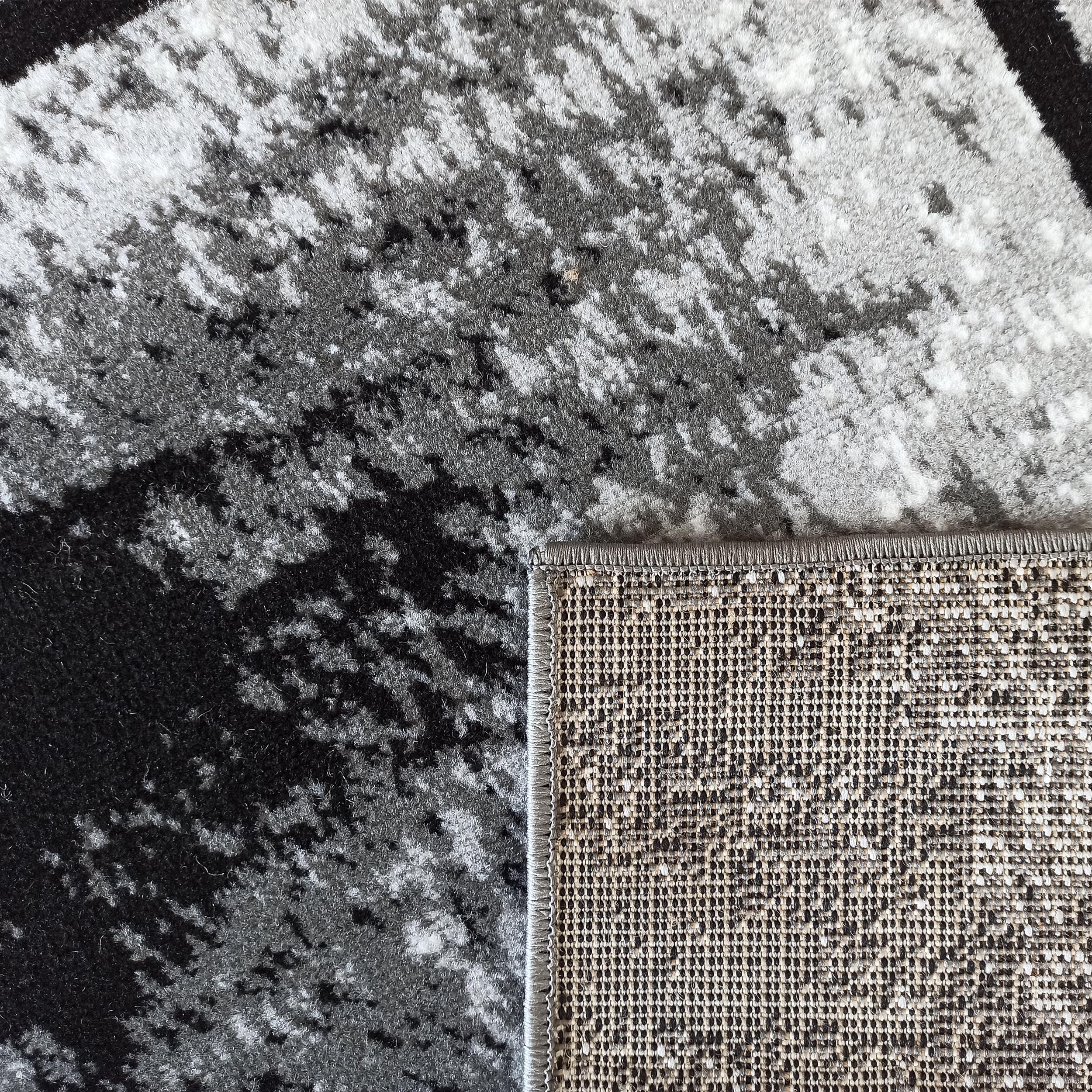 Tapis doux aux motifs abstraits noirs, gris et blancs en gros plan, montrant l'envers tissé beige et marron