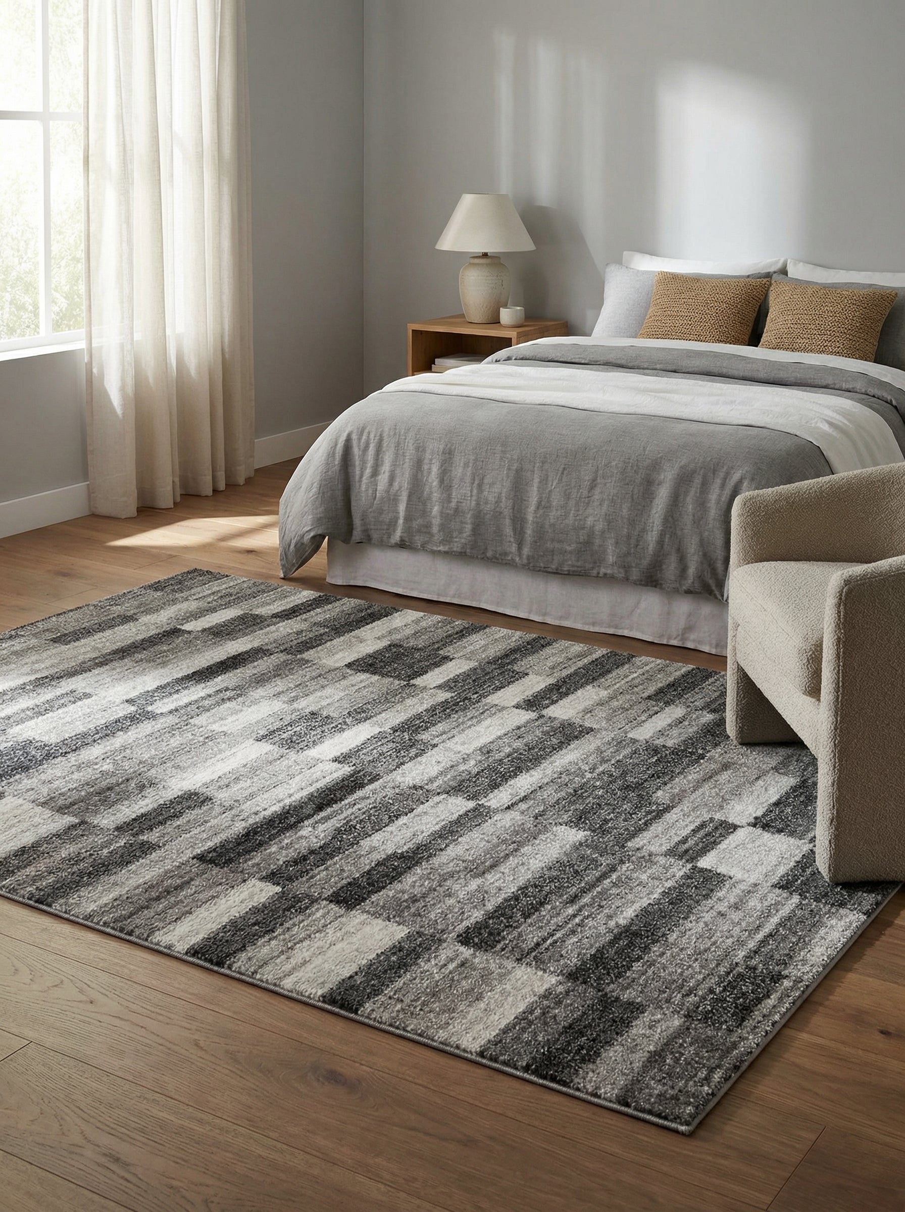 Tapis rectangulaire gris et blanc aux motifs géométriques abstraits en bandes diagonales, posé sur un parquet dans une chambre lumineuse